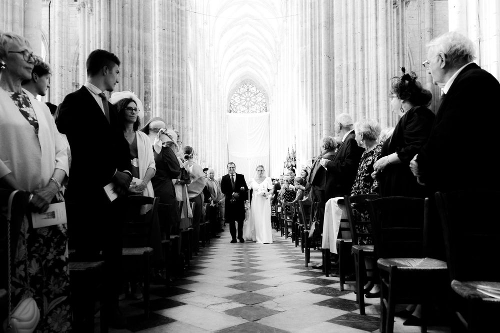 Black and white wedding ceremony photo inside a grand cathedral with bride and groom walking down the aisle.