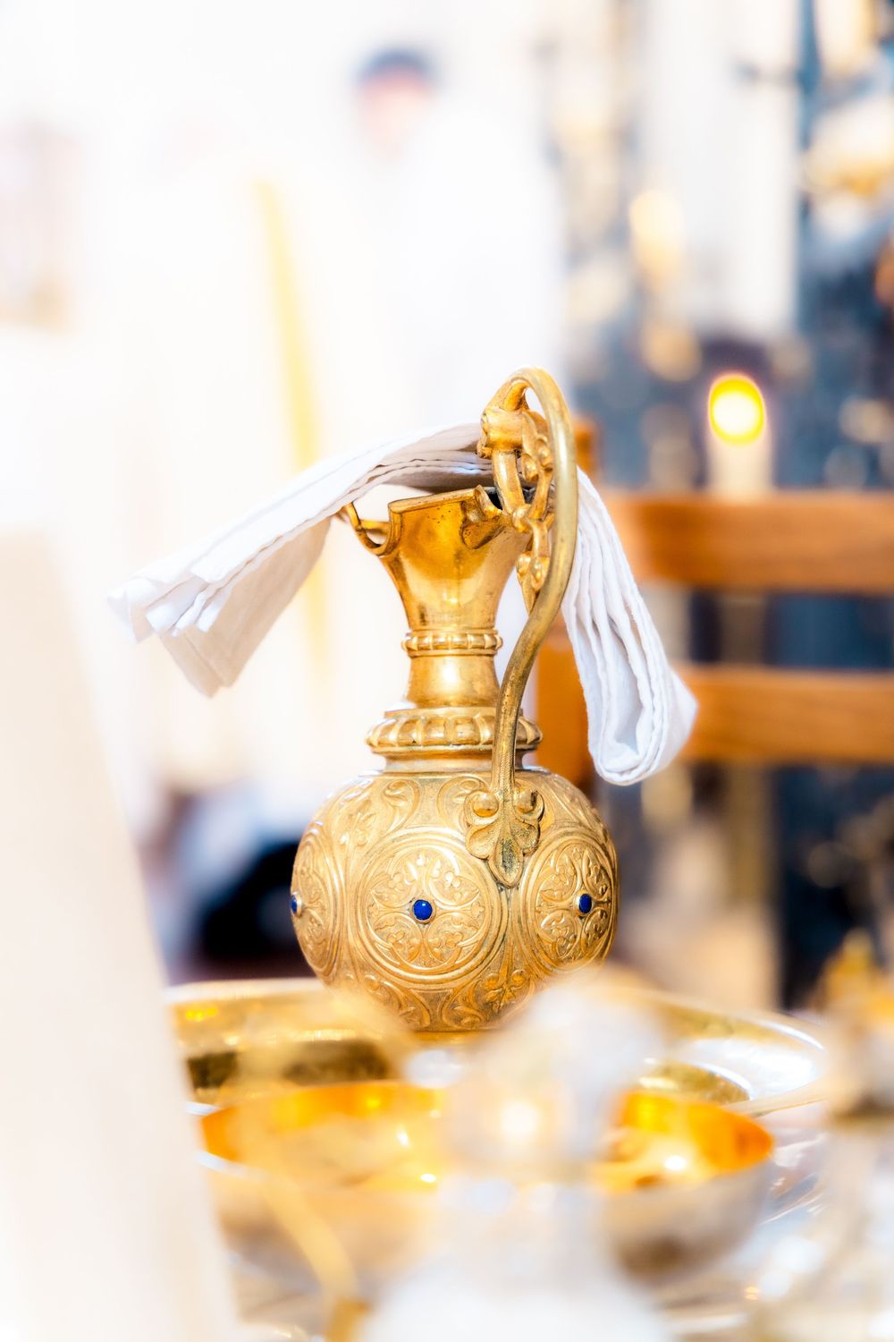 Ornate golden ceremonial ewer with blue gemstones and white ribbon on a church altar table.