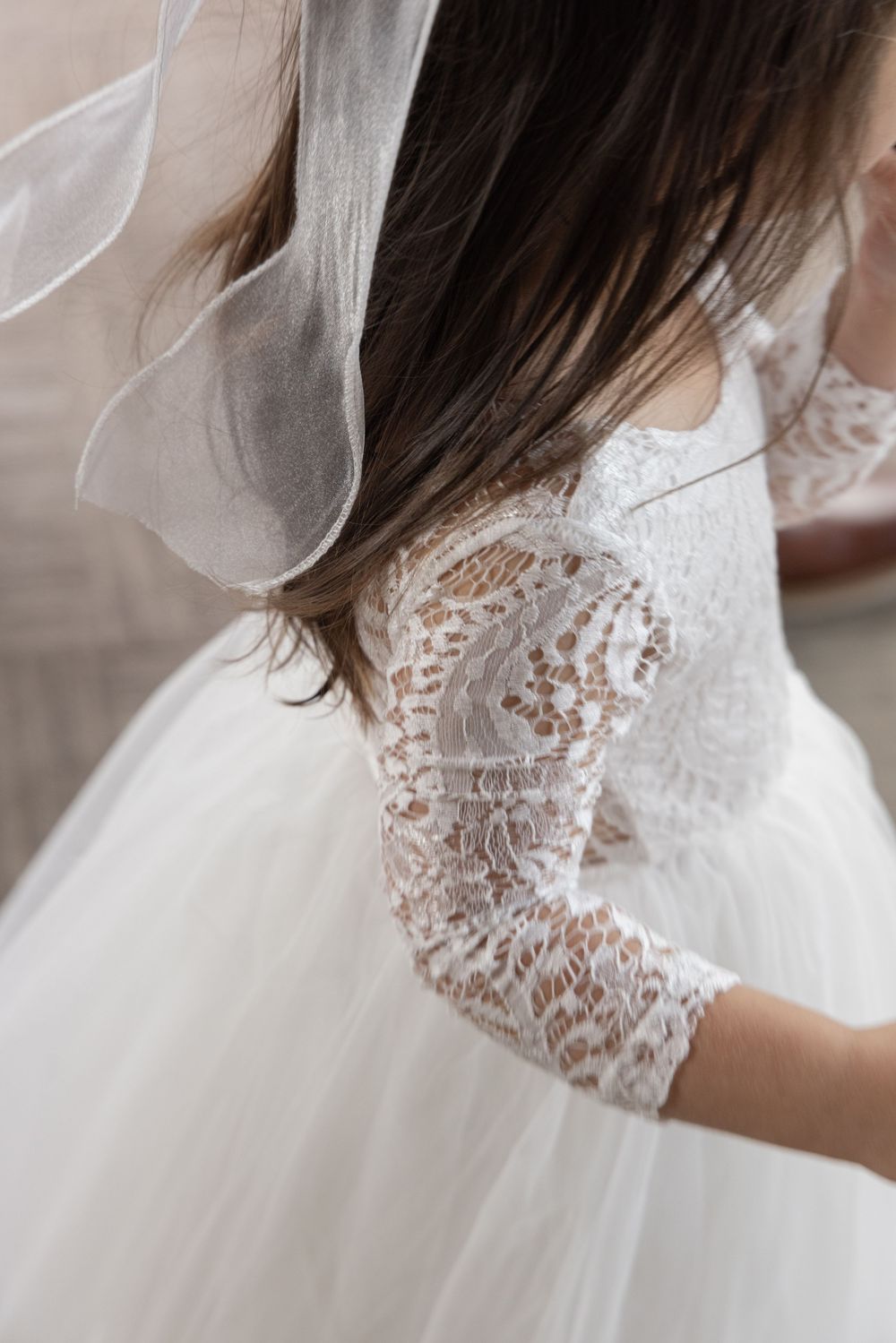 Young girl in white lace flower girl dress with tulle skirt and veil, elegant back detail view.