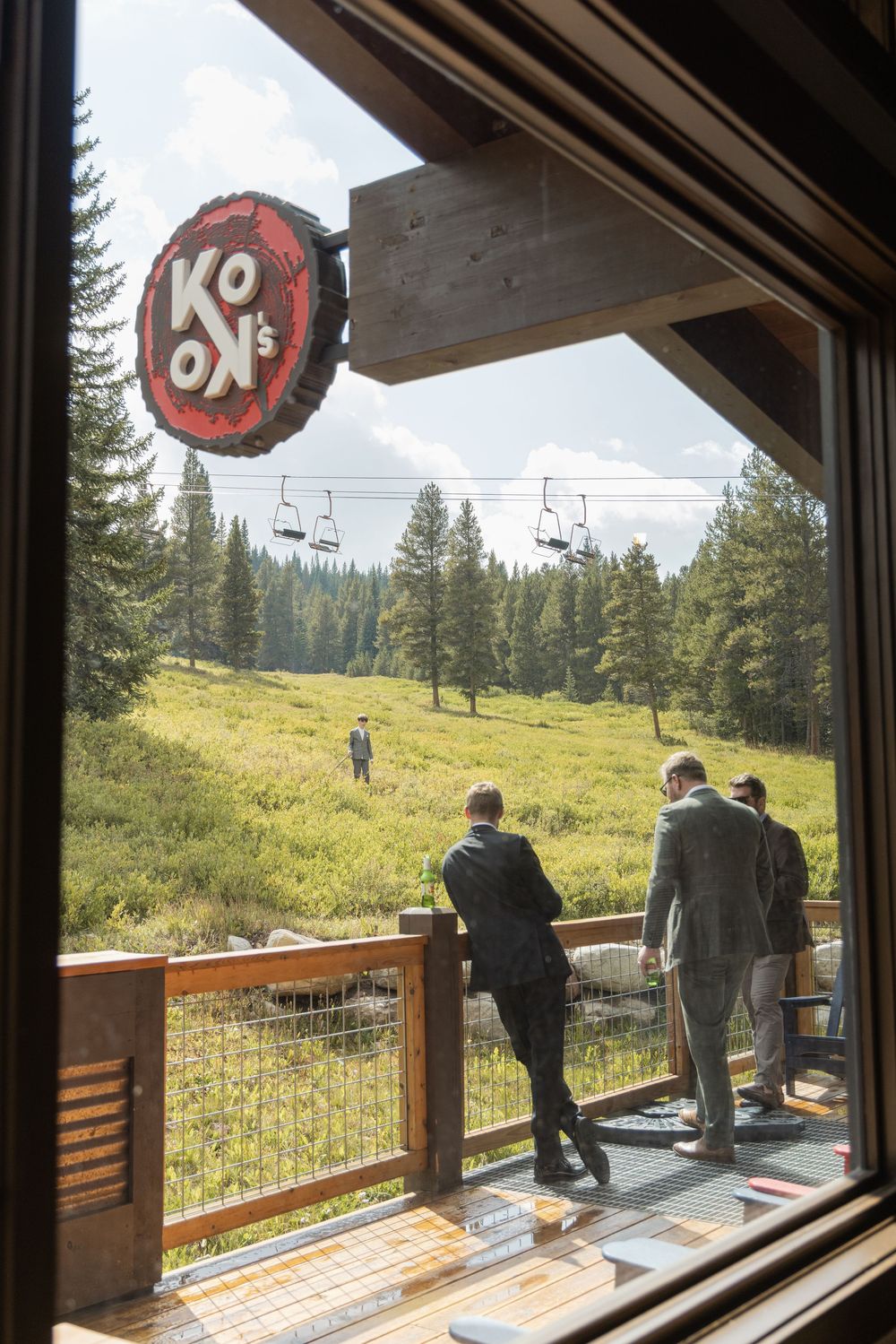 View through window of Koon's restaurant deck overlooking scenic mountain meadow with ski lift and pine trees.