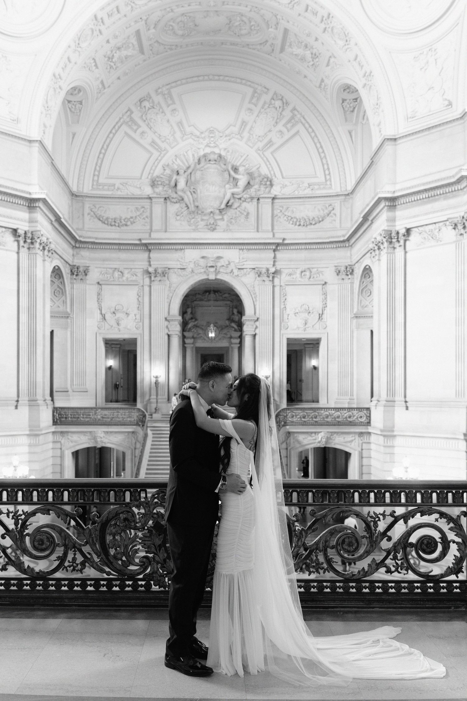 Black and white photo of a couple sharing a kiss at San Francisco City Hall, bride in flowing gown with veil.