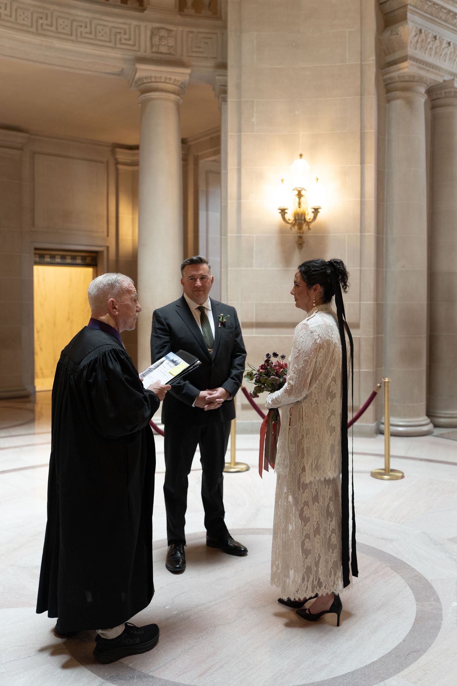 Couple exchanging vows with officiant at San Francisco City Hall wedding ceremony in elegant marble rotunda.