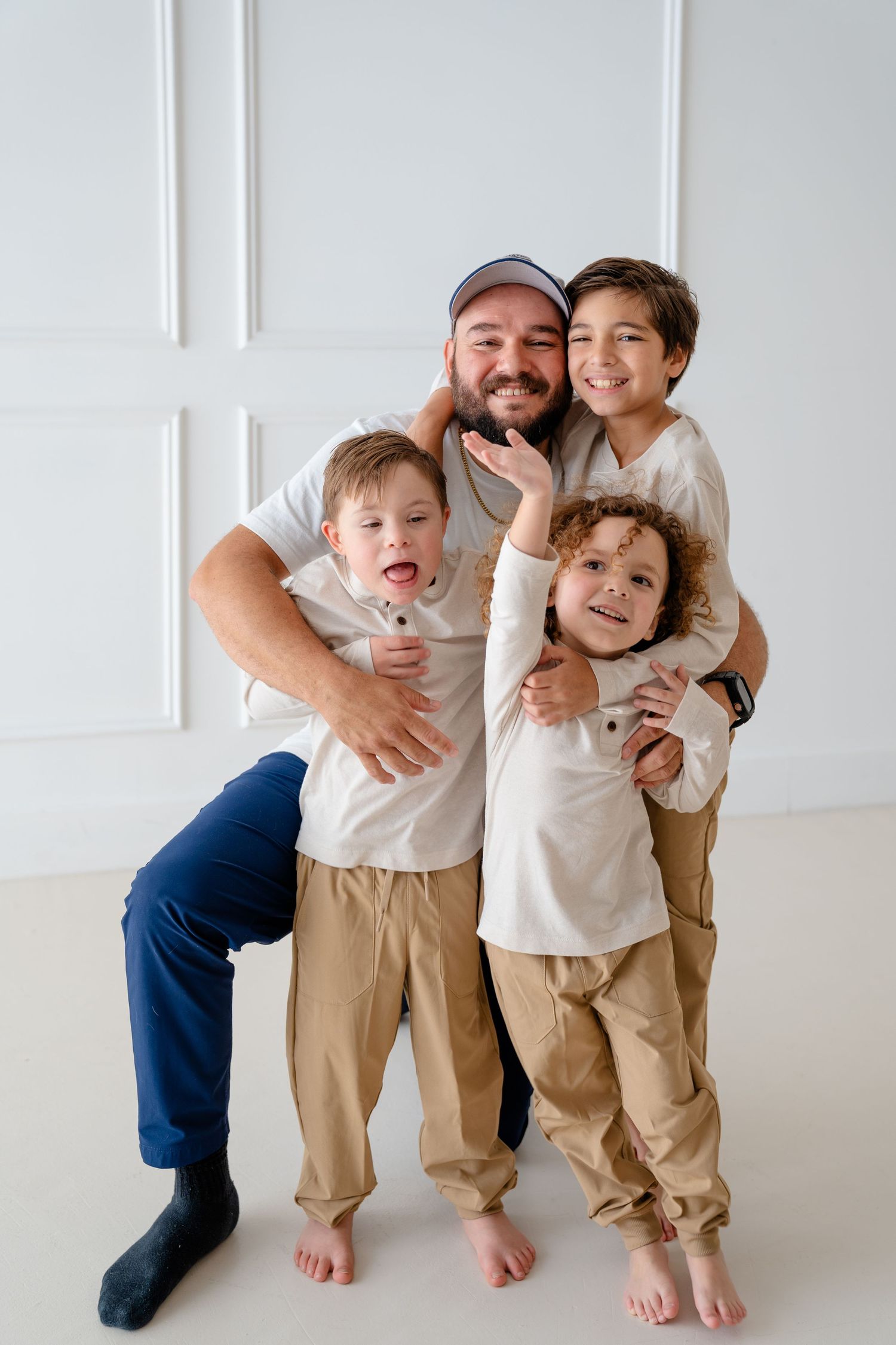 A father sitting on the floor hugging and kissing his young toddler daughter in a bright white room.
