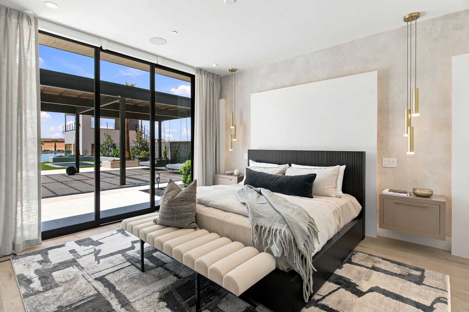 Modern primary bedroom with black-framed sliding glass doors opening to a covered patio and pool