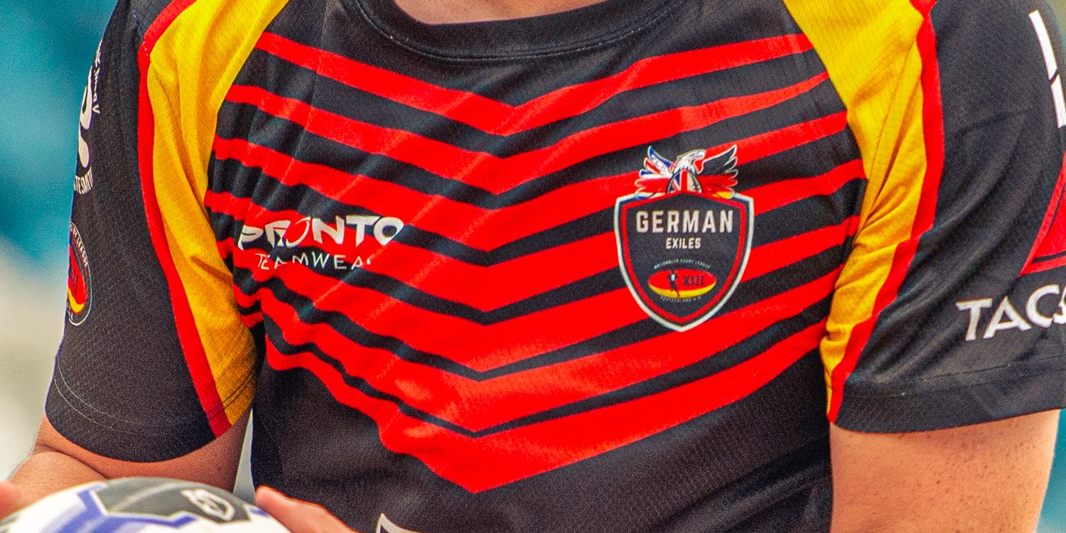 German rugby league player holding ball in red and black striped jersey with eagle crest badge closeup.