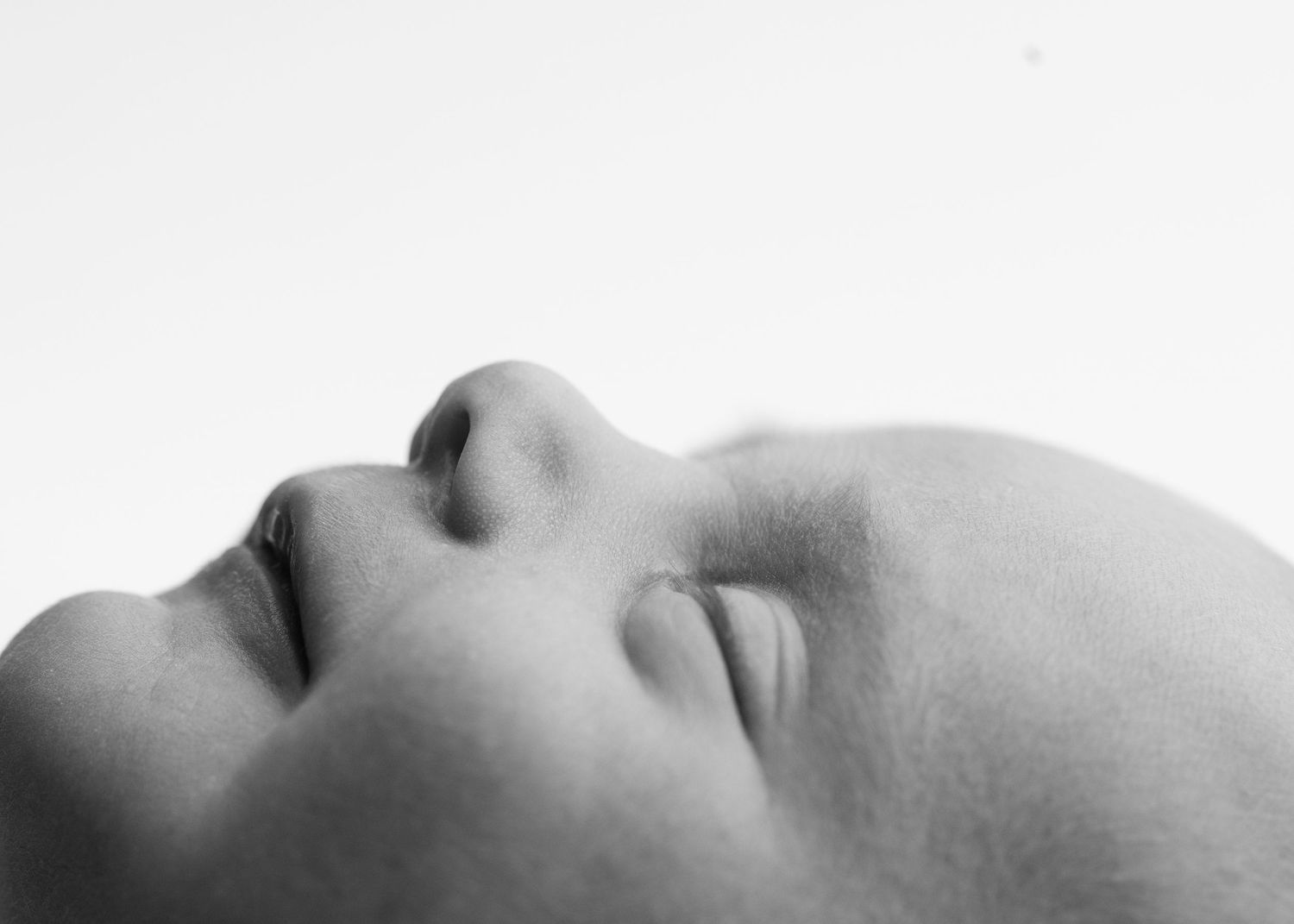 Close-up black and white photo of a sleeping baby's serene face tilted upward against a white background.