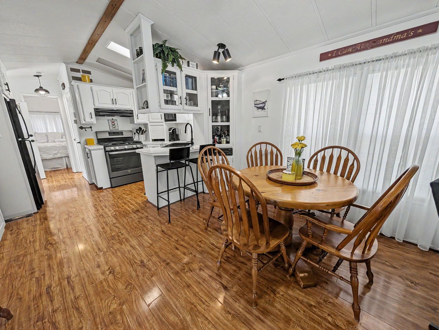 Bright dining area with round wood table, Windsor chairs, and hardwood floors open to a white kitchen with bar seating.