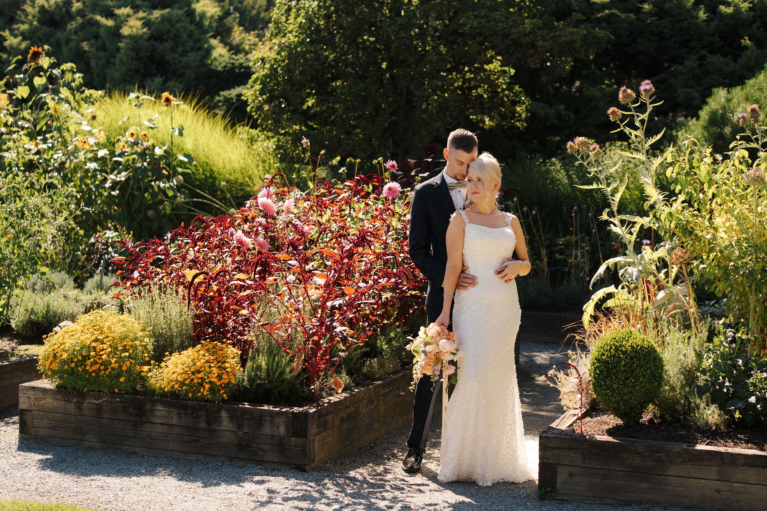 Wedding couple sharing a tender moment surrounded by vibrant autumn garden beds in warm sunlight.