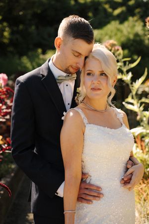 Newlywed couple poses tenderly in a sunlit garden, bride in sequined gown.