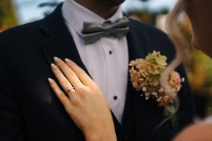 Close-up of bride's hand with wedding ring resting on groom's black tuxedo lapel.