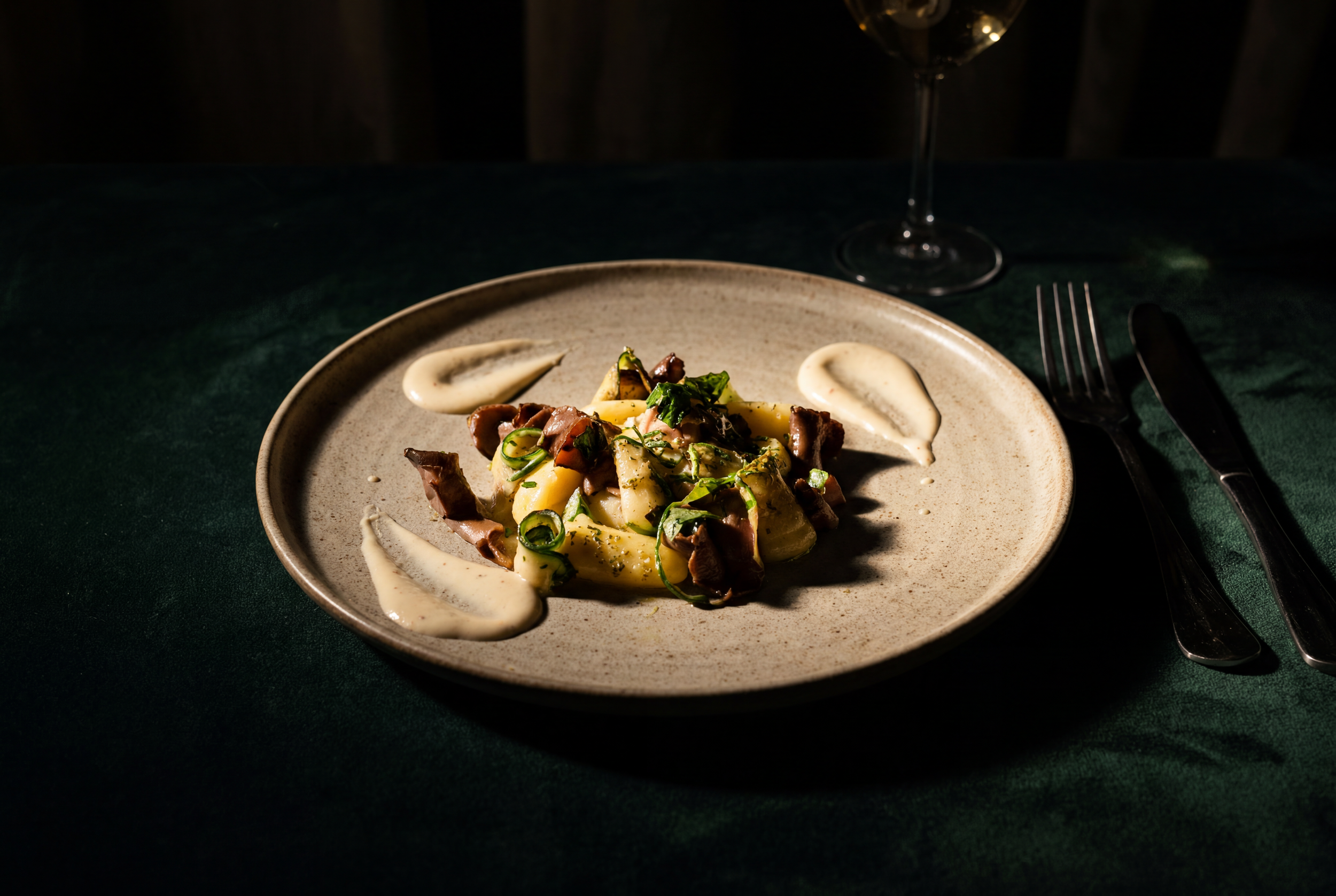 Elegant gourmet dish with gnocchi, mushrooms, and cream sauce on a ceramic plate in moody restaurant lighting.