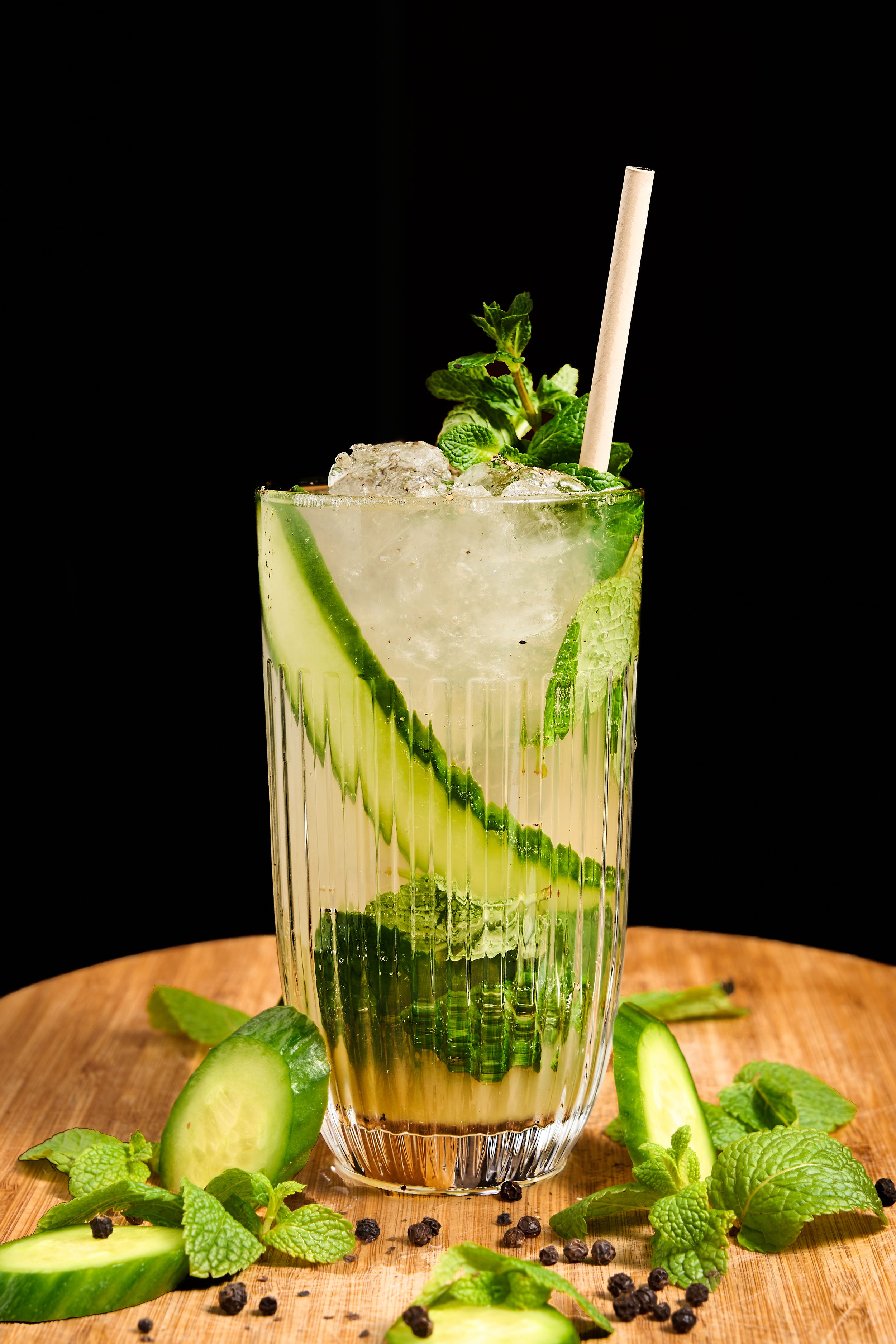 Refreshing cucumber mint mojito cocktail with ice, garnished with fresh mint leaves and cucumber slices on wooden board.