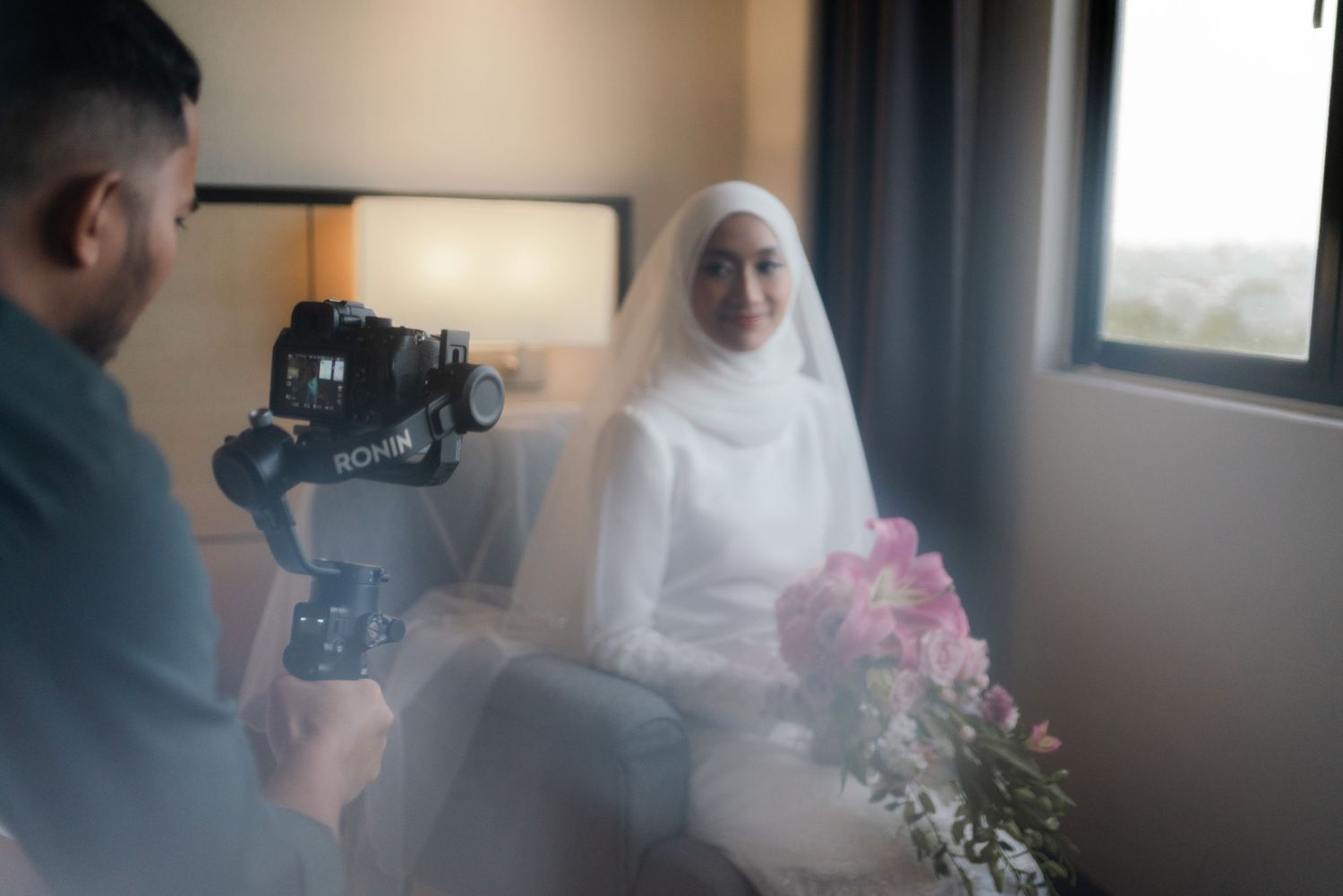 A photographer captures footage of a bride holding pink flowers in a room.