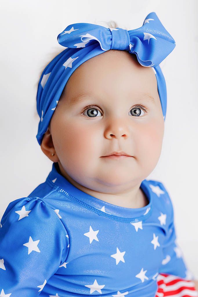 Cute baby girl wearing a blue star-print outfit by affordable baby photographer in Riverside county.