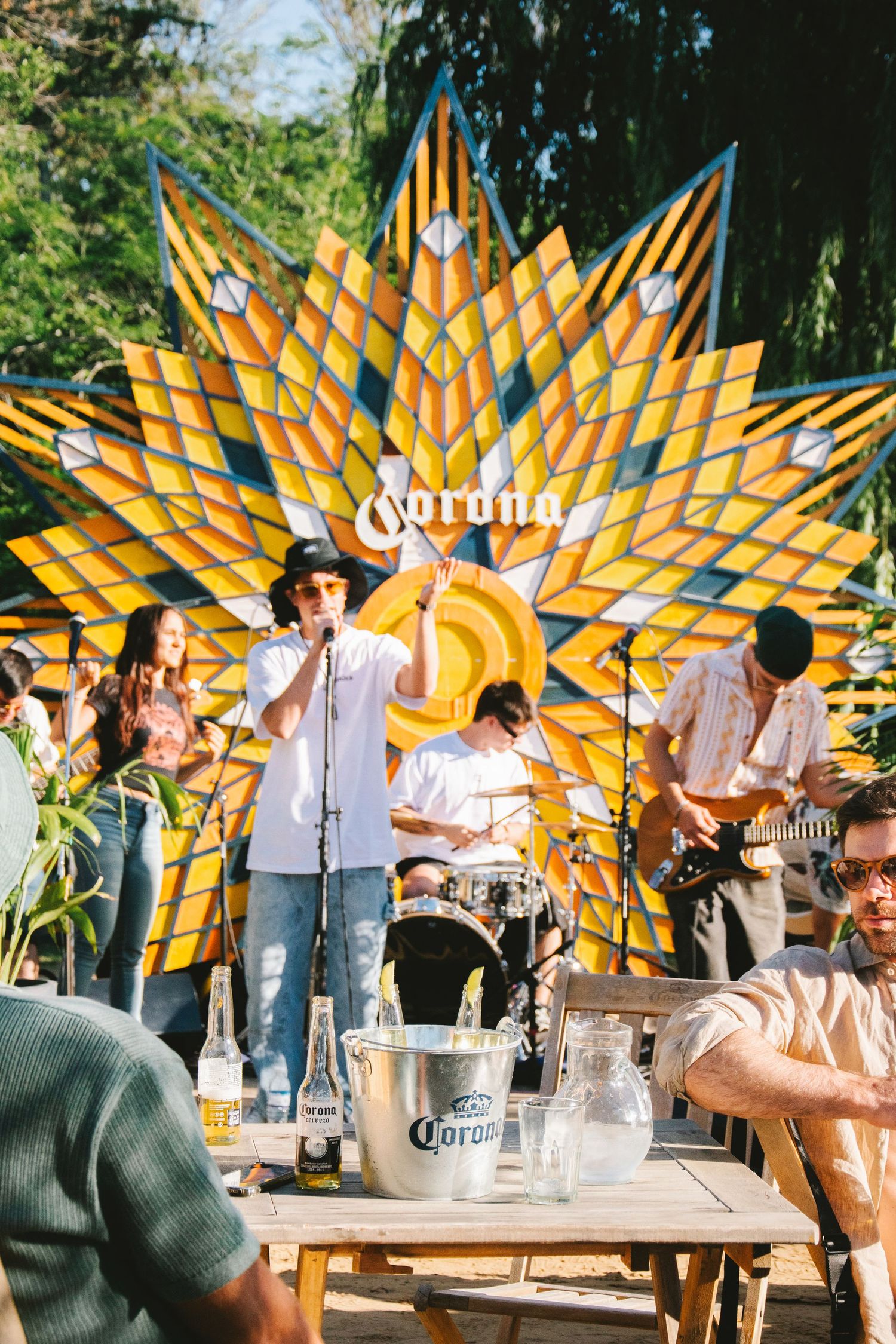 Band performing live on a Corona-branded sunburst stage at an outdoor festival event.