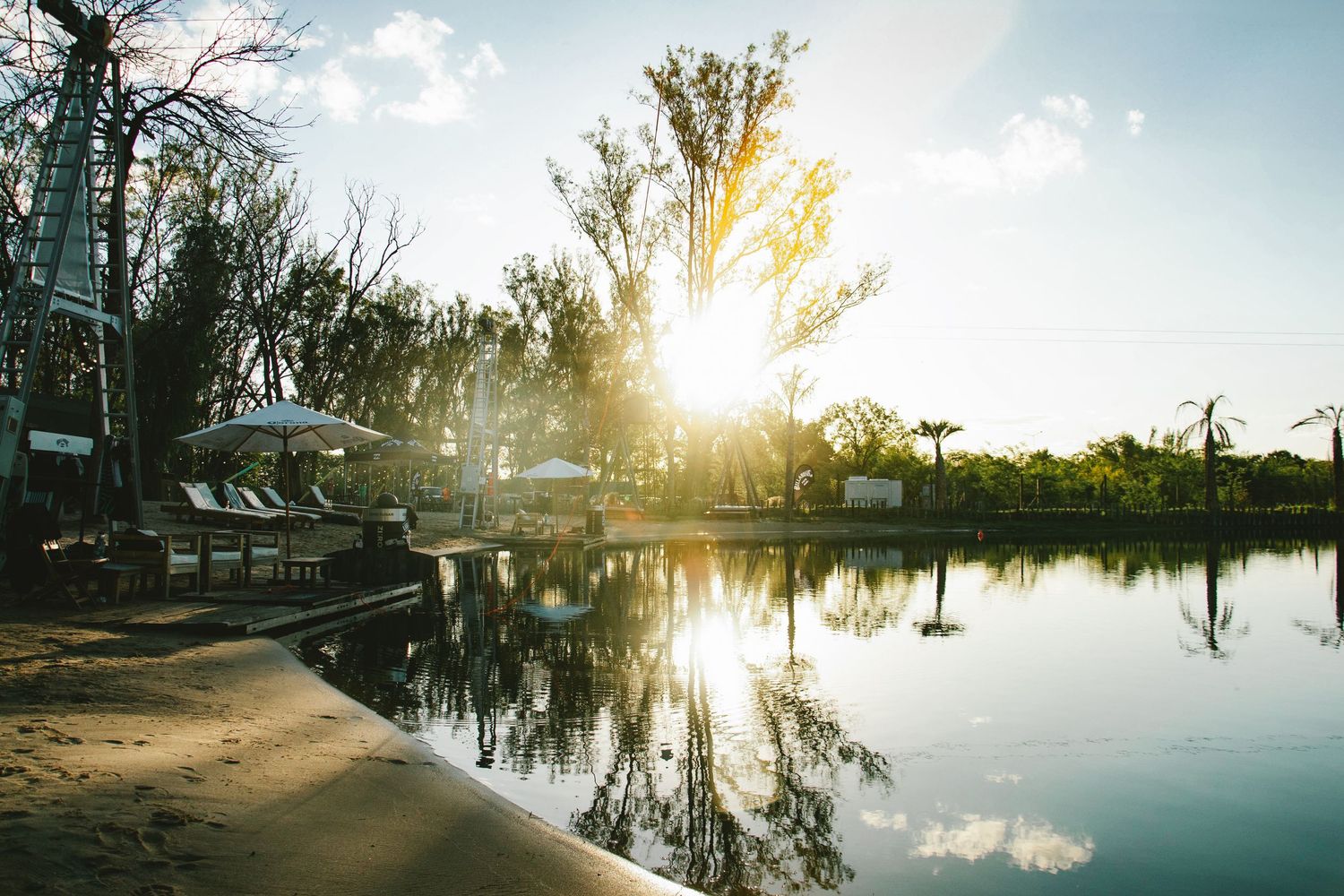 Golden sunset reflecting over a calm lake at an outdoor venue surrounded by lush trees.
