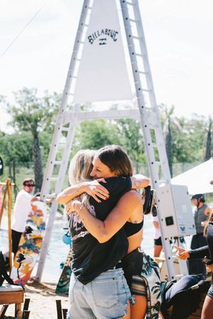 Two people hugging at a Billabong outdoor event near a lake.