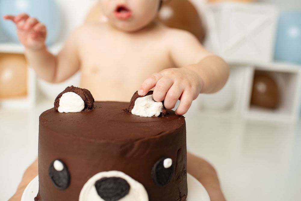 Baby reaching into a chocolate bear-themed birthday cake with cream decorations.