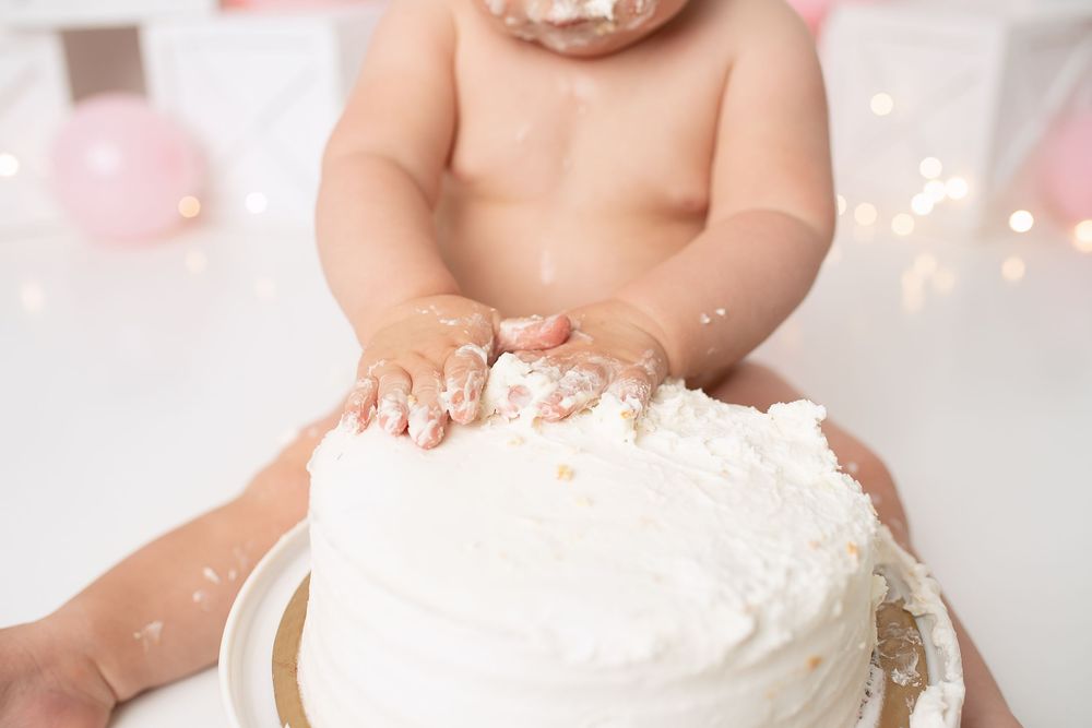 Close-up of baby hands smashing white frosted cake during first birthday cake smash photo session.
