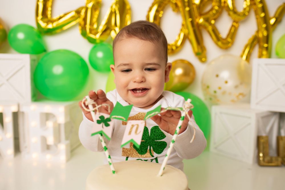 Happy baby reaching into a St. Patricks Day themed birthday cake with green and gold decorations.