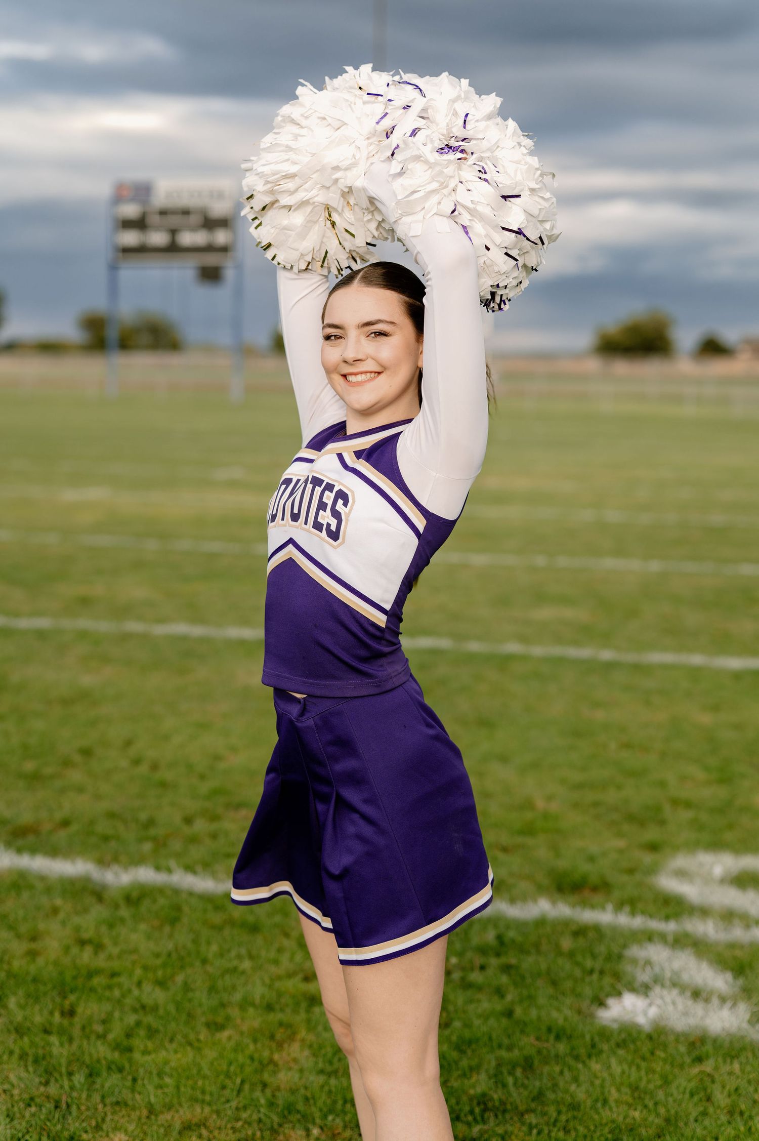 A 2026 senior on her high school football field in her cheer uniform with poms