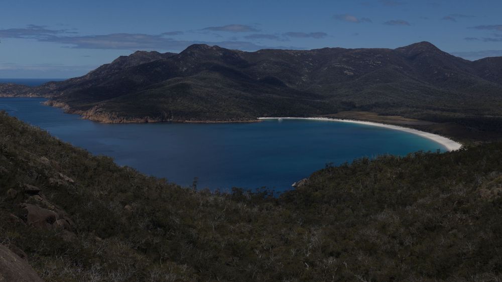 Aerial panoramic view of Wineglass Bay in Tasmania with turquoise waters and green mountain surrounds.