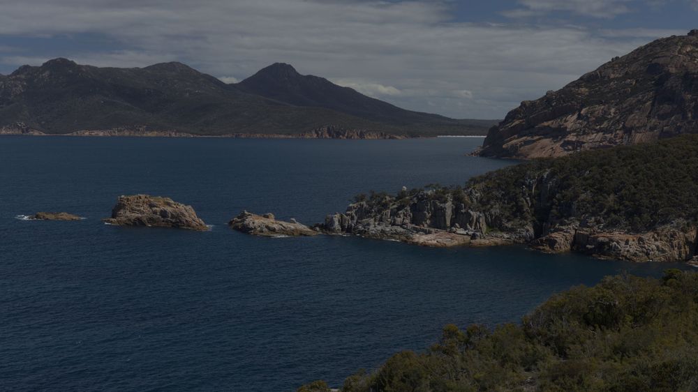 Rocky coastal landscape with deep blue waters and mountain peaks in Freycinet National Park.