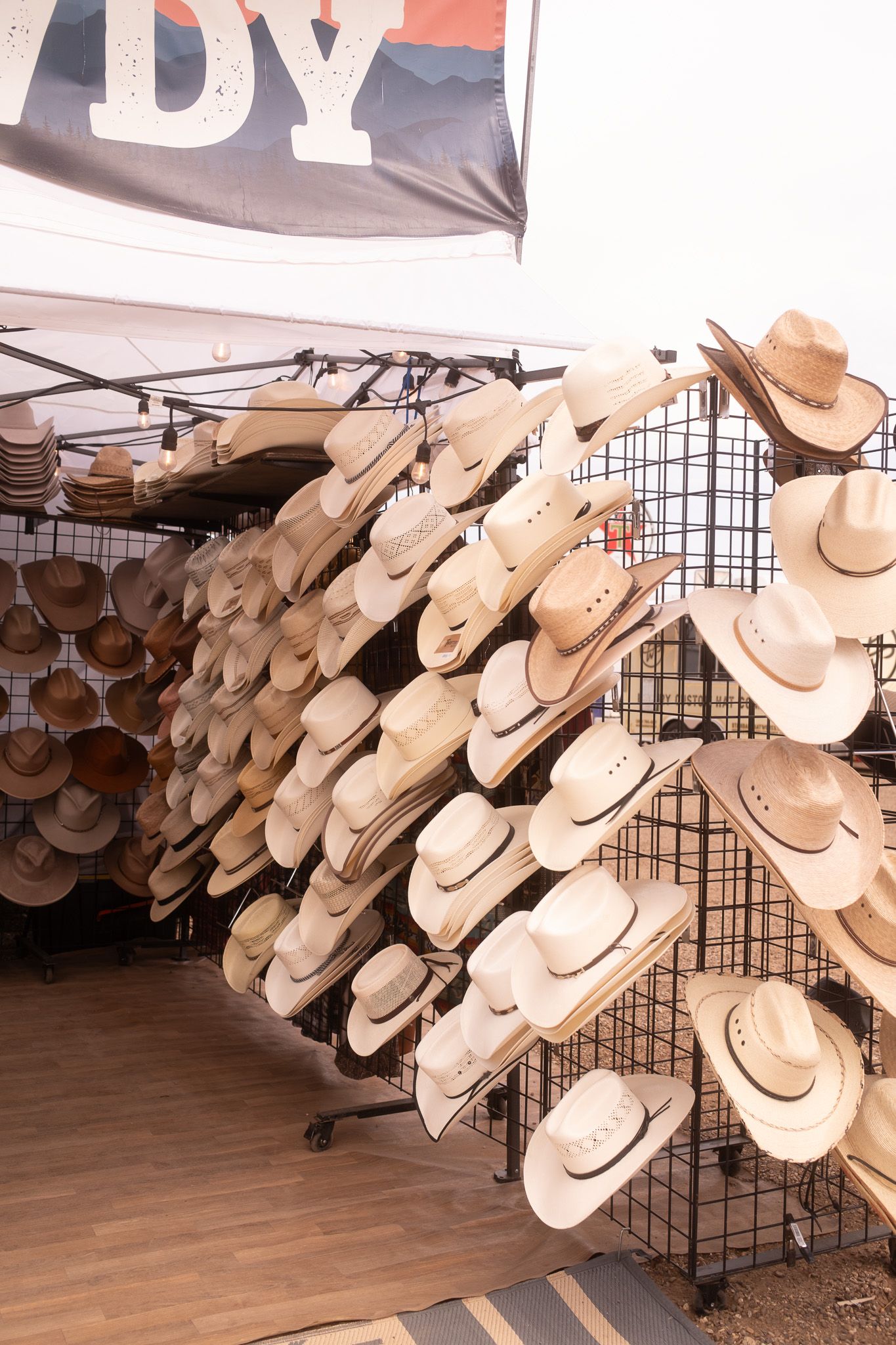 Rows of cowboy hats displayed on racks at an outdoor western vendor booth with a HOWDY banner.