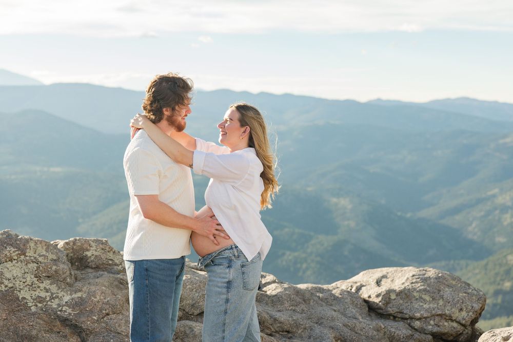 Couple embracing on a rocky mountain summit with scenic blue ridge mountain views in the background.