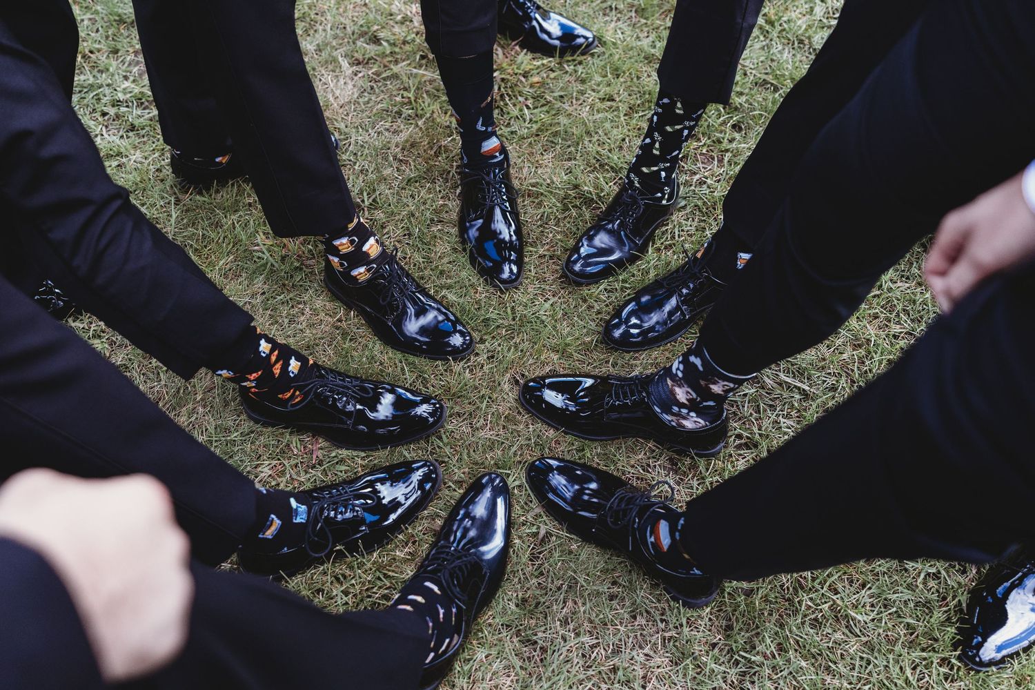 Overhead view of groomsmen in a circle showing off their matching black patent leather dress shoes on grass.