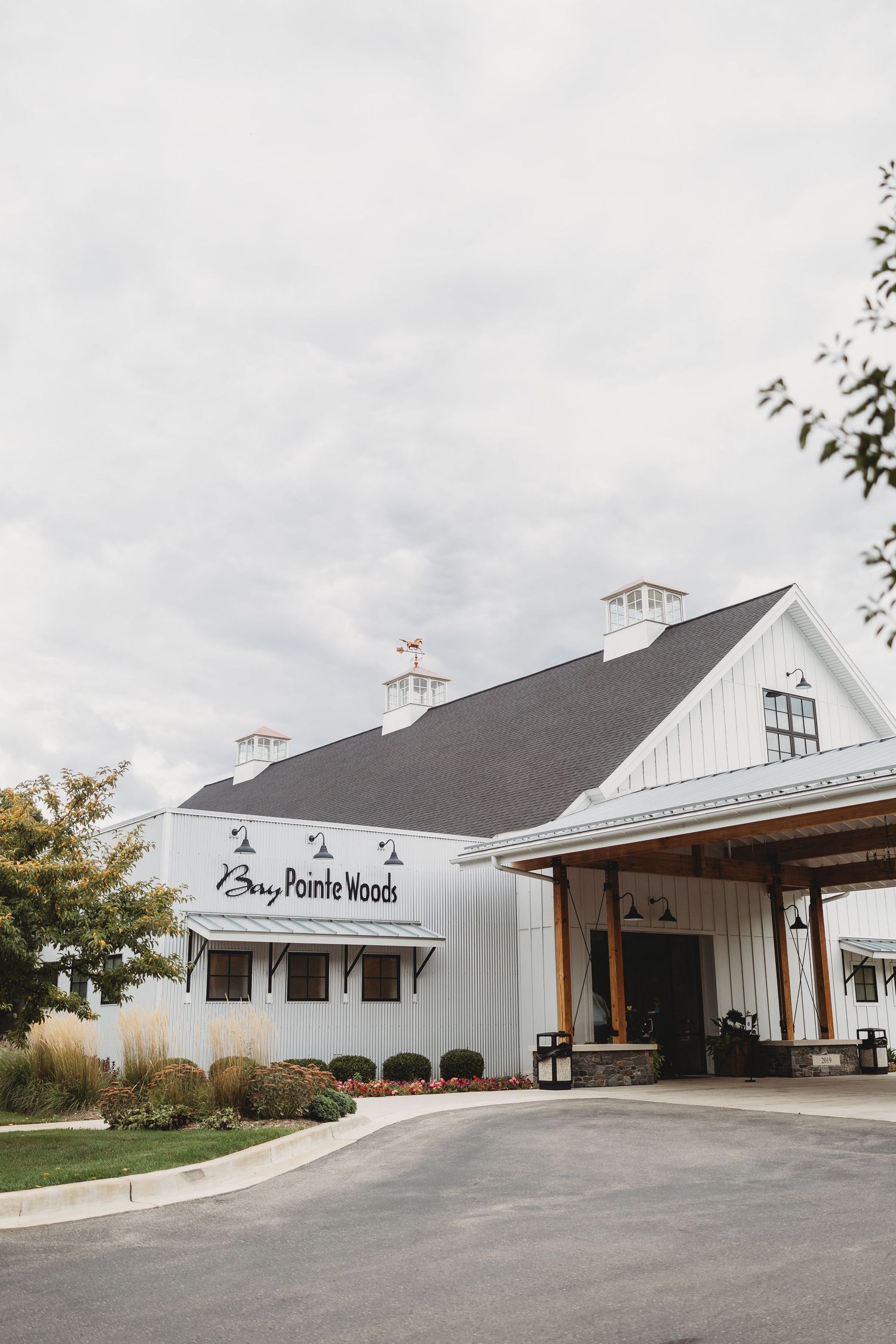 Bay Pointe Woods wedding venue exterior featuring white barn architecture with dark roof and covered entrance.