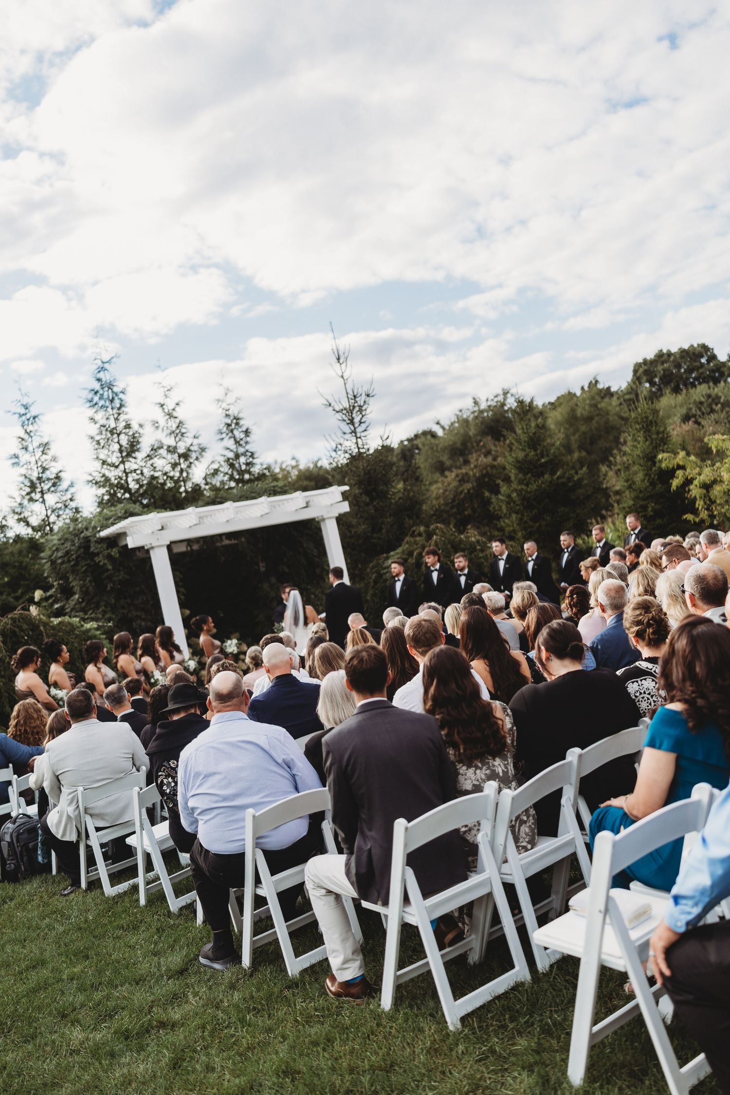 Outdoor wedding ceremony with guests seated on white chairs facing altar.