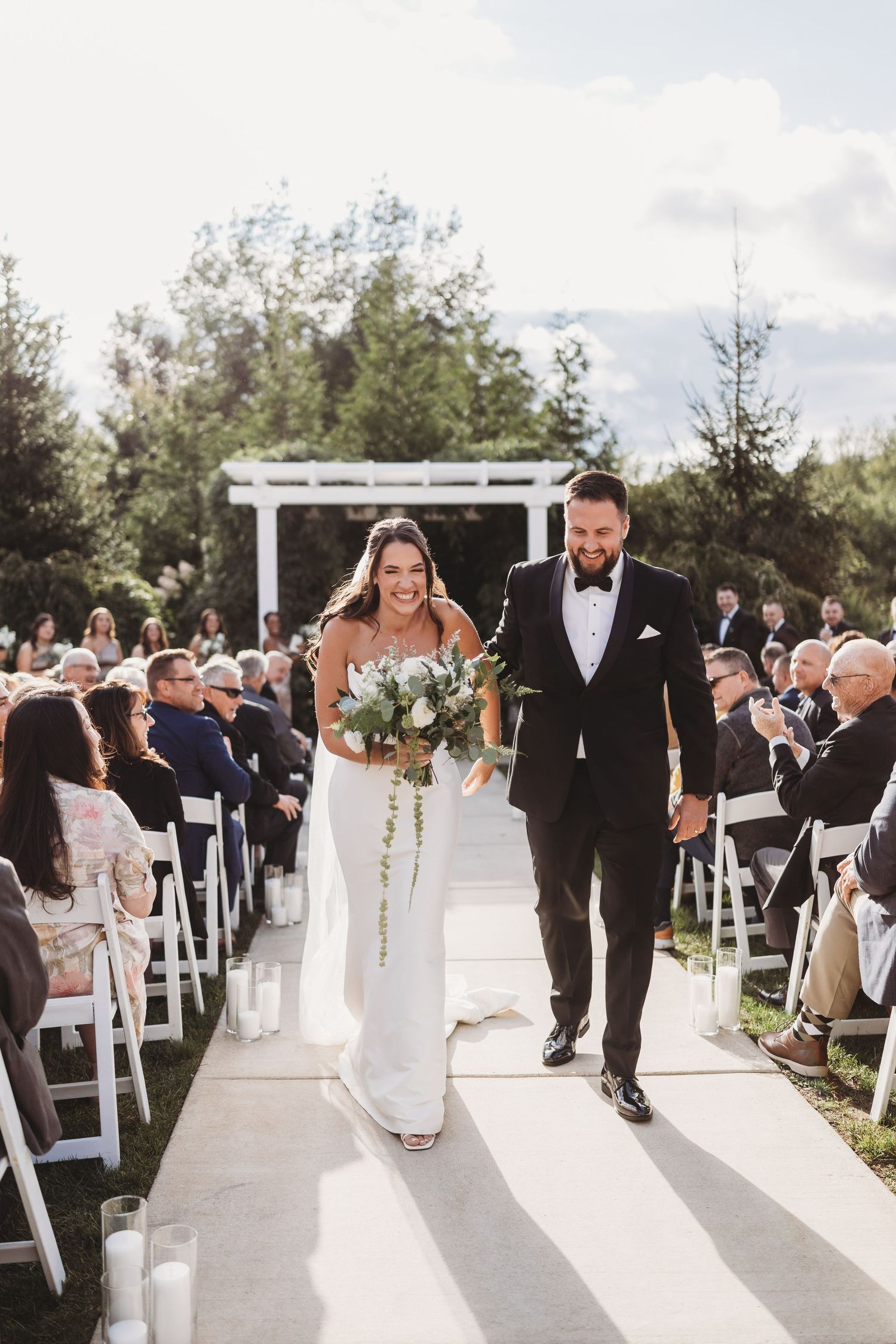 Newlyweds walking back down the aisle after outdoor wedding ceremony with guests seated.