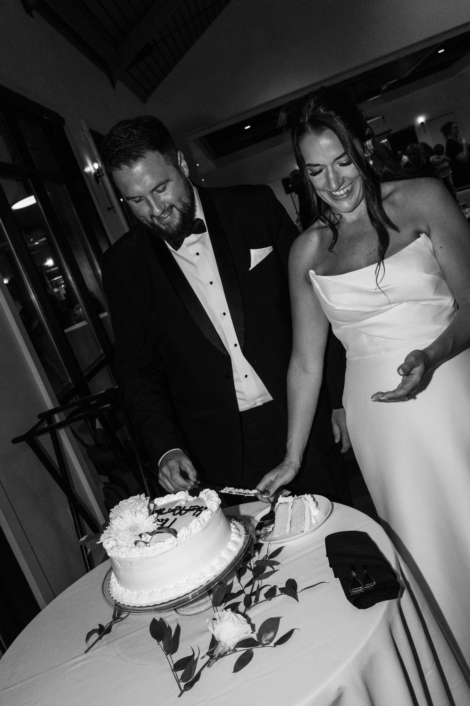 Bride and groom cutting their white wedding cake together in black and white photo.