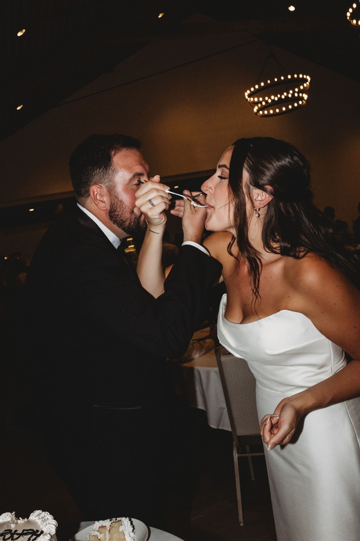 Bride and groom sharing intimate wedding cake cutting moment in dimly lit reception venue.