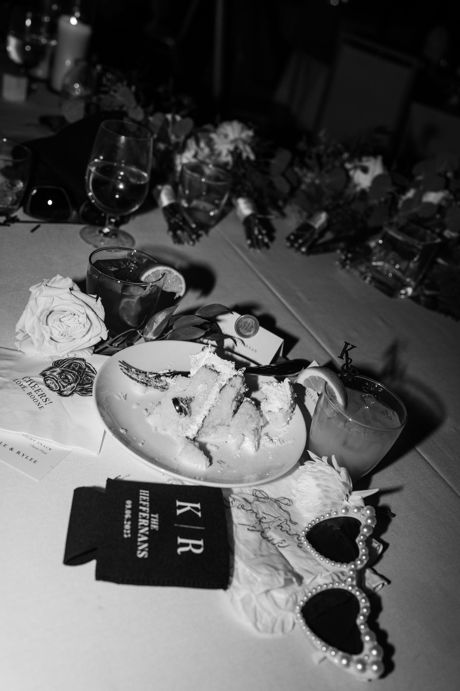 Black and white wedding table with cake, pearl sunglasses, K|R koozie, roses, and glassware at the Ruttermans reception.