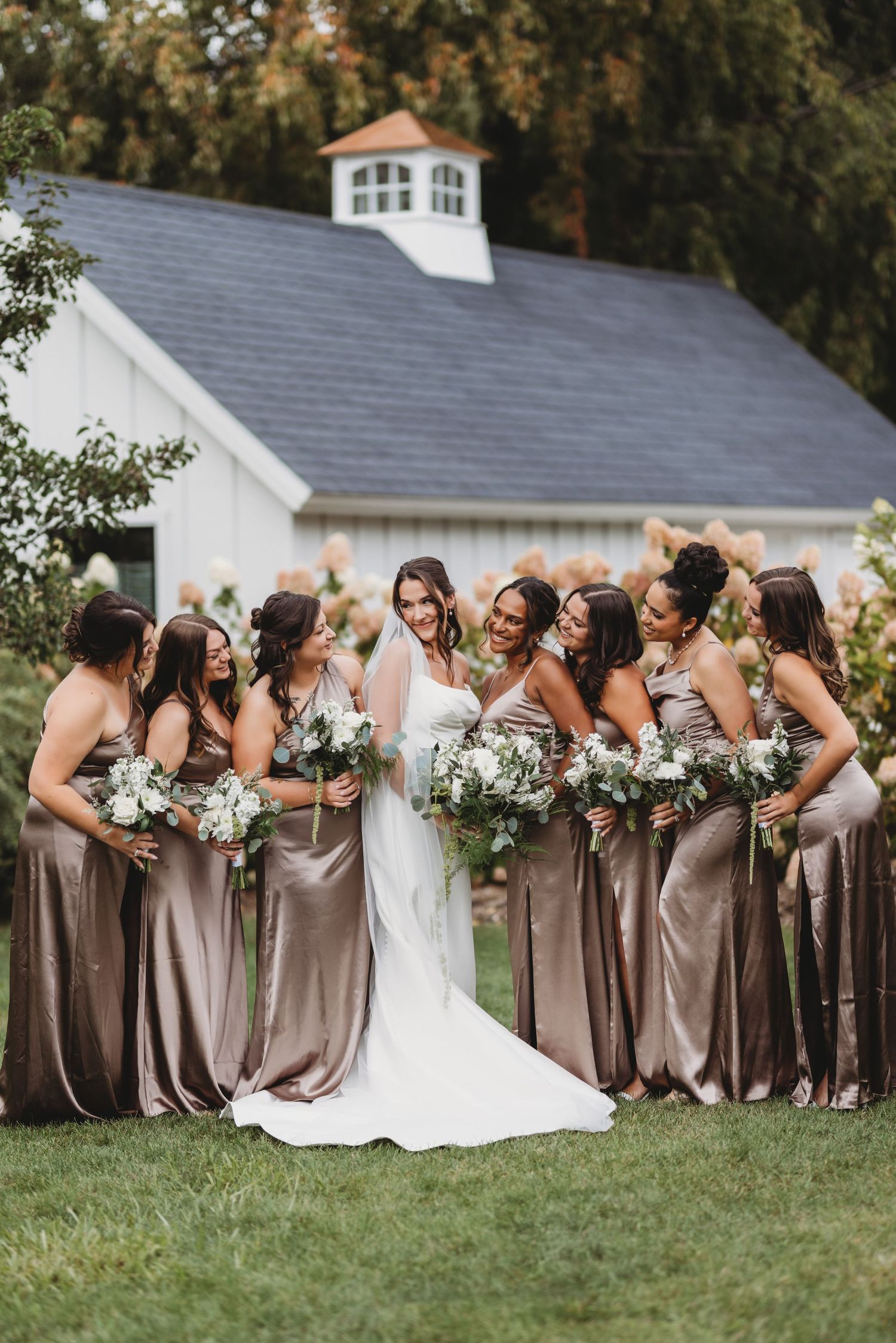 Bride surrounded by bridesmaids in champagne satin gowns holding white bouquets.