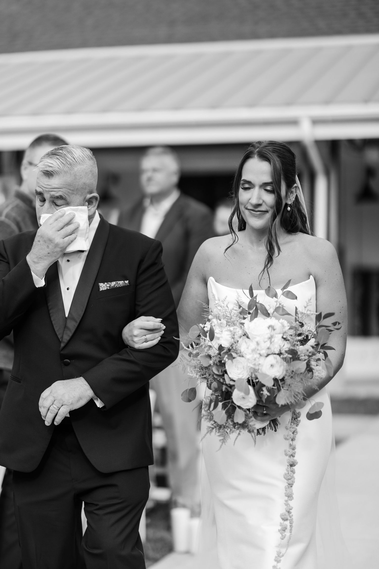 Emotional father walks bride down aisle as she smiles holding floral bouquet.