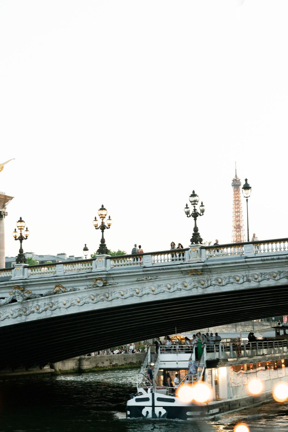 Pont Alexandre III bridge over Seine River in Paris with ornate lampposts, passing boat, and Eiffel Tower at dusk. paris film photographer