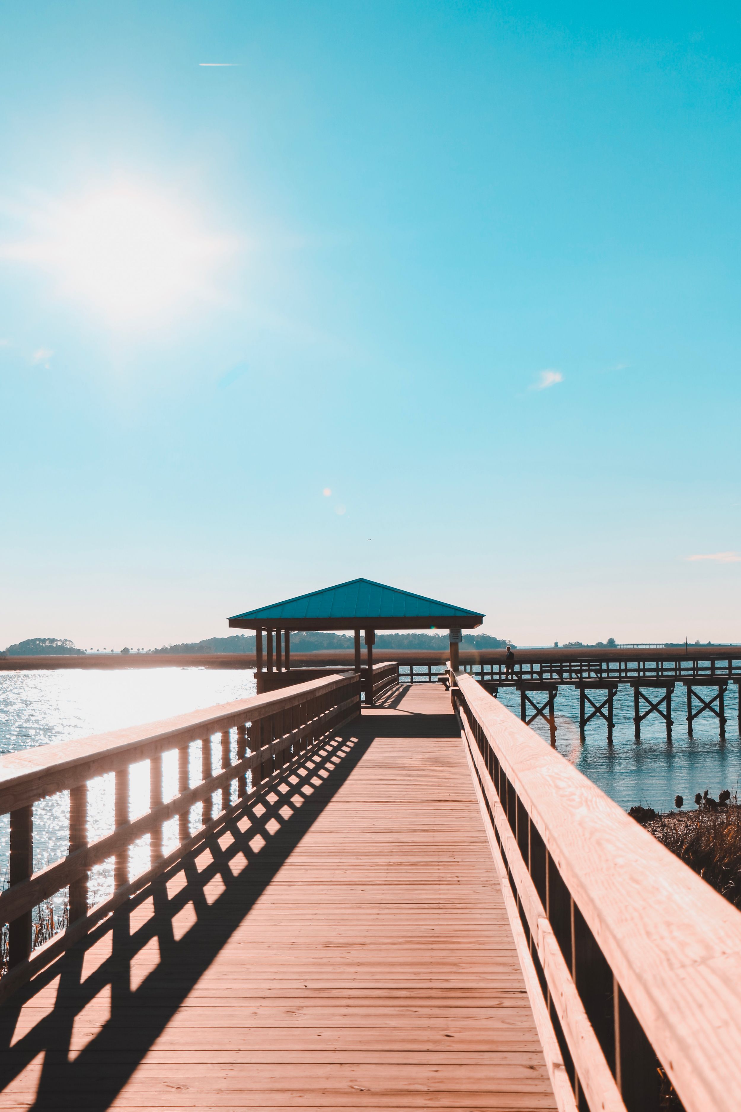 Long wooden pier walkway with covered gazebo extending over calm water at sunrise.