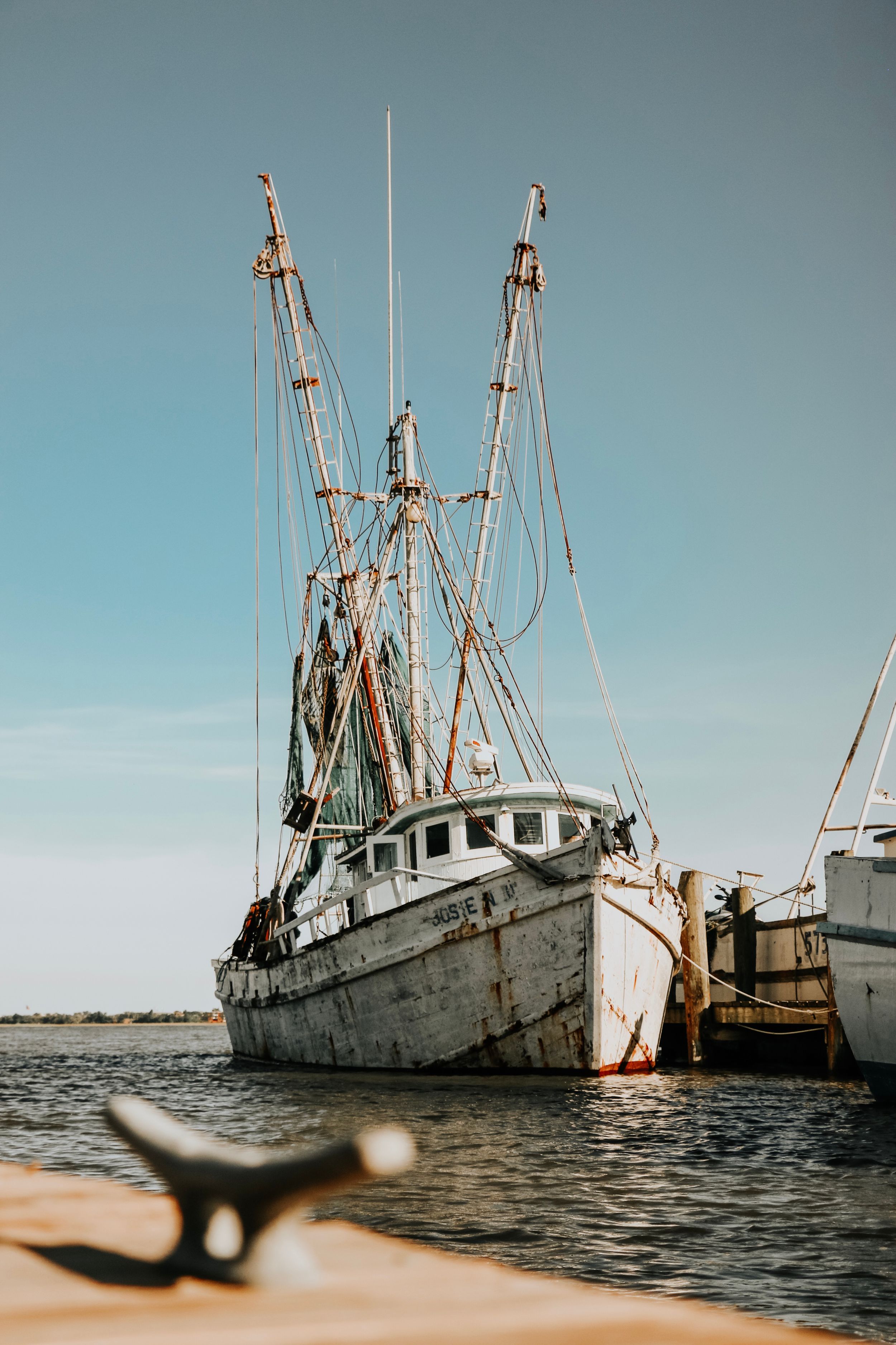 Weathered fishing boat with tall masts docked in calm waters on a sunny day.