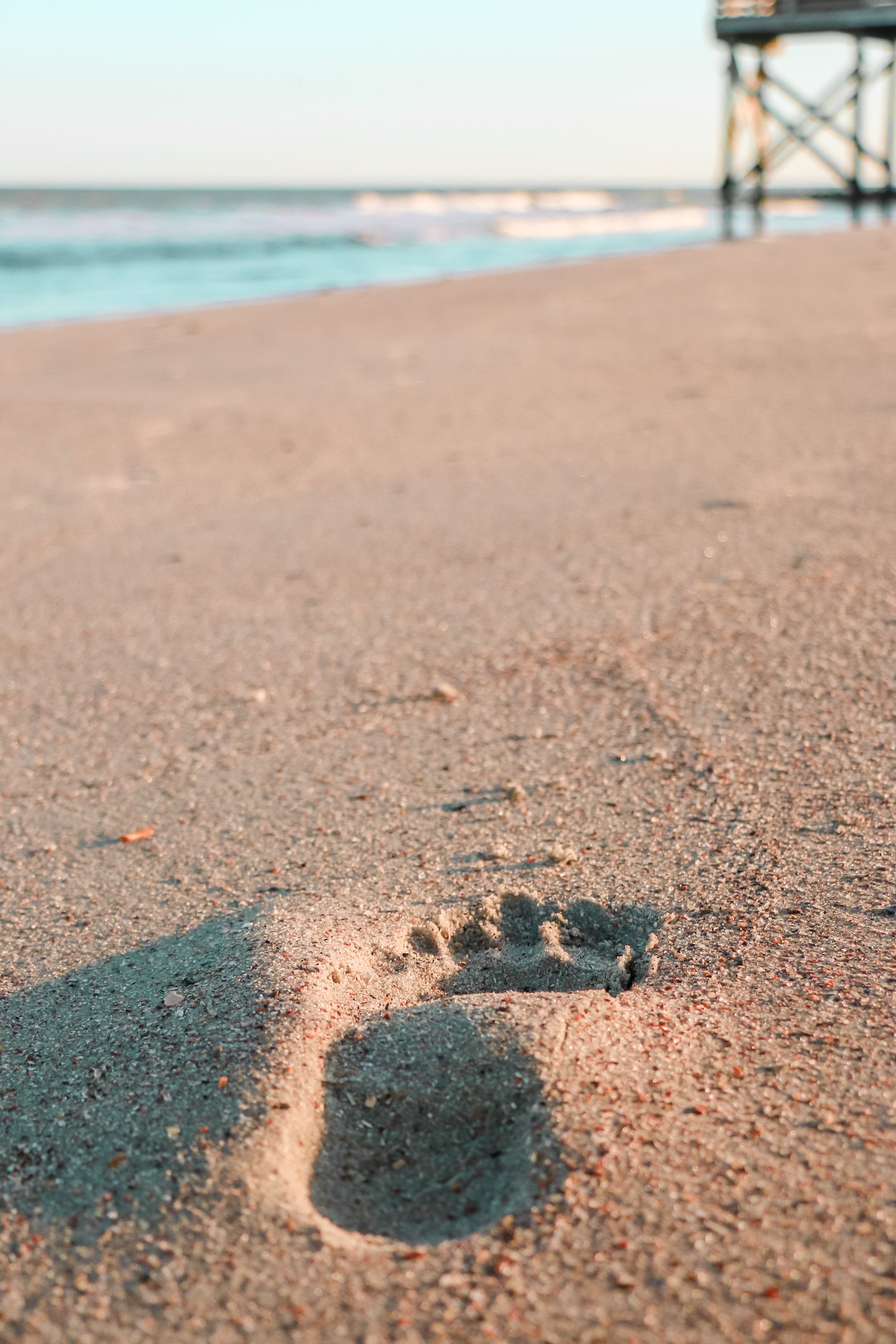 Single footprint impression in sandy beach near wooden pier at sunset.