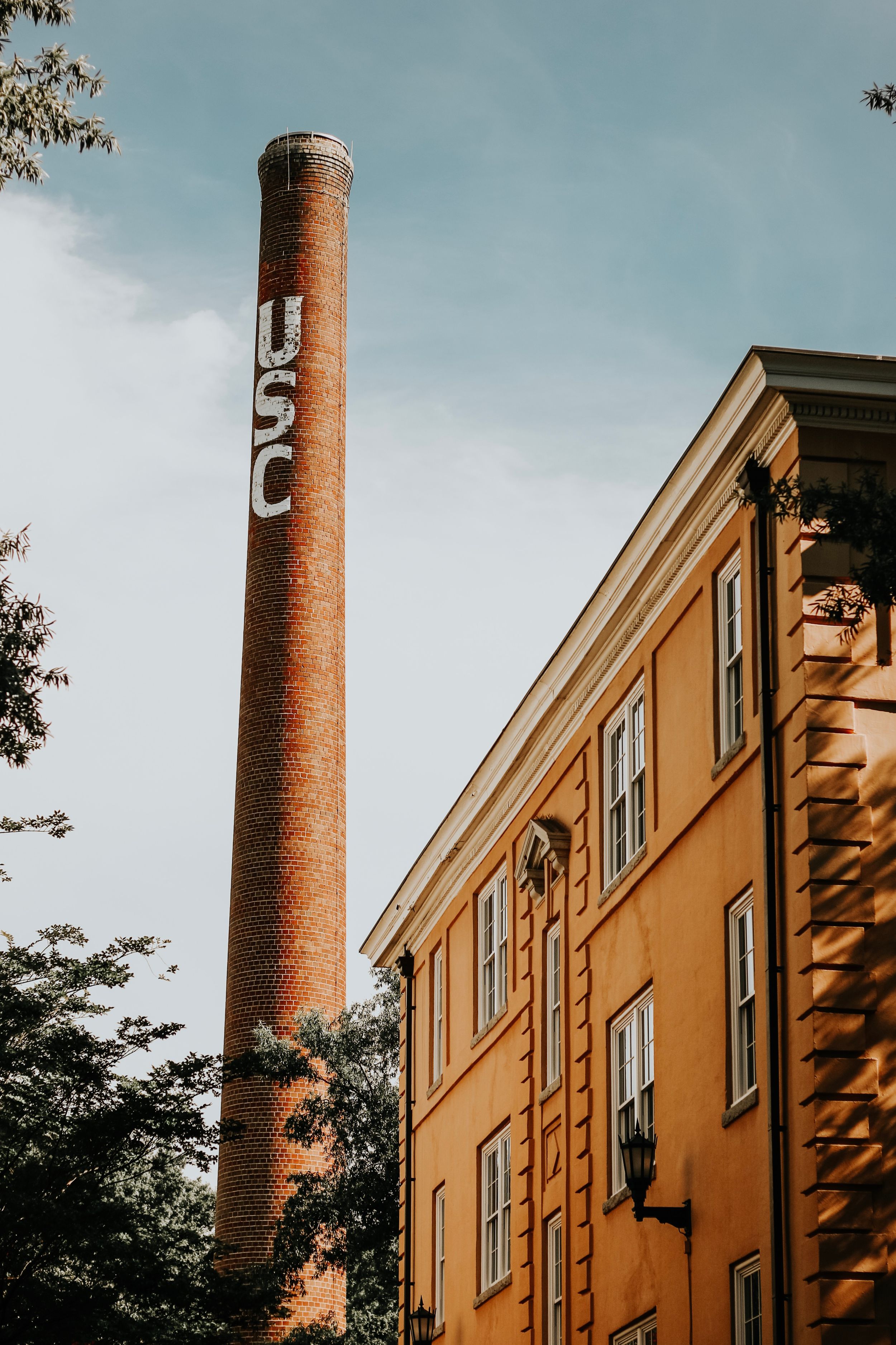 Historic brick smokestack with painted lettering next to yellow industrial building.
