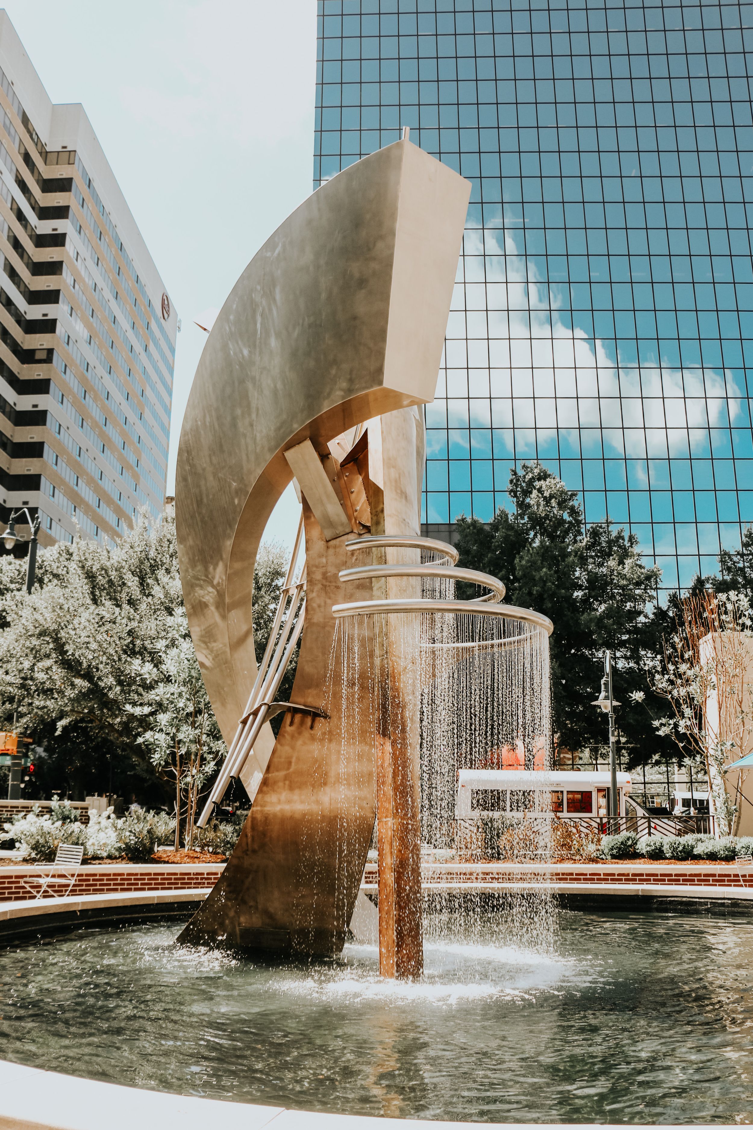 Modern curved metal fountain sculpture in front of glass office building.