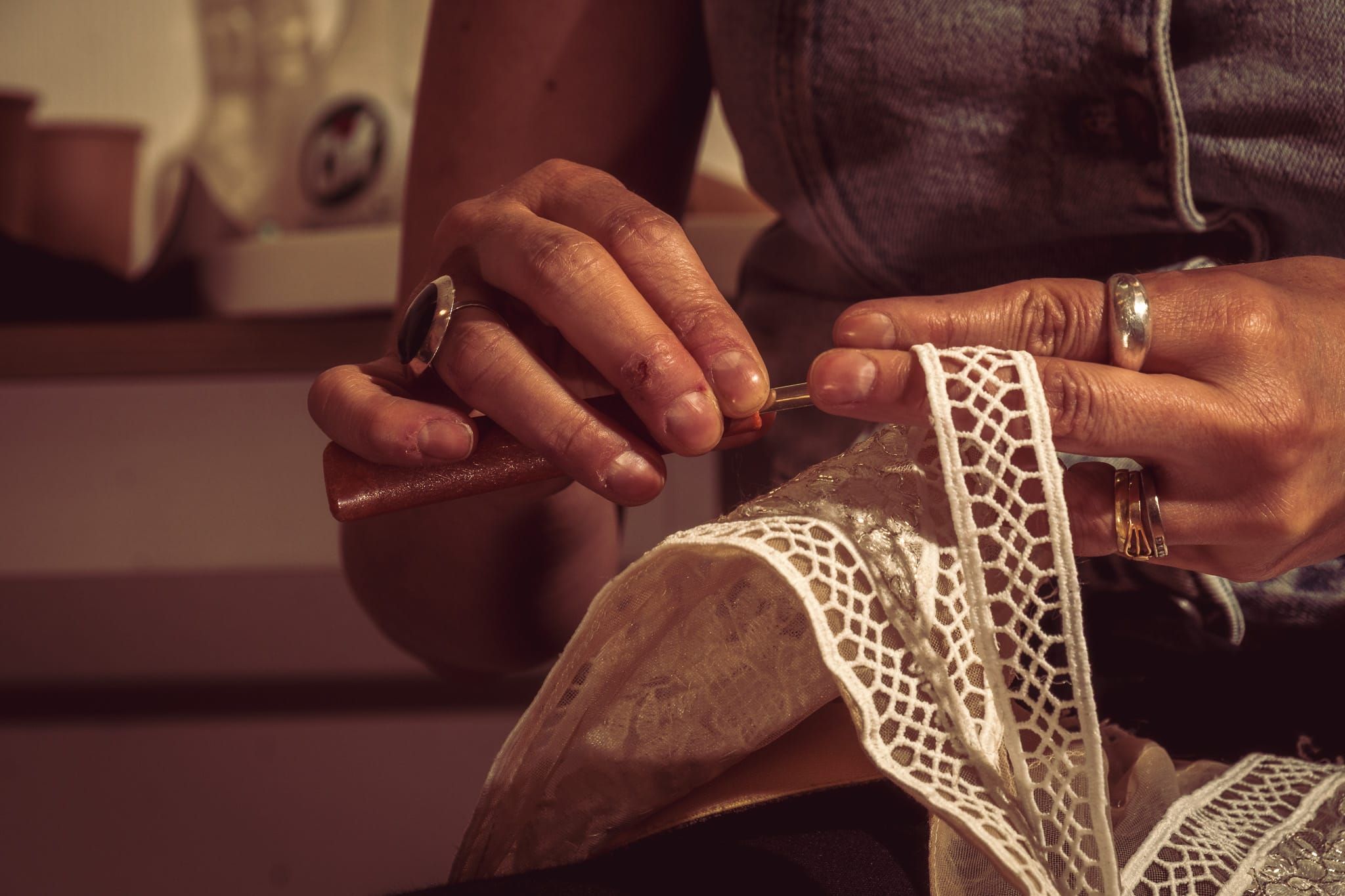 Close-up of hands crafting delicate white lace trim with a needle and thread, showcasing traditional needlework skills.