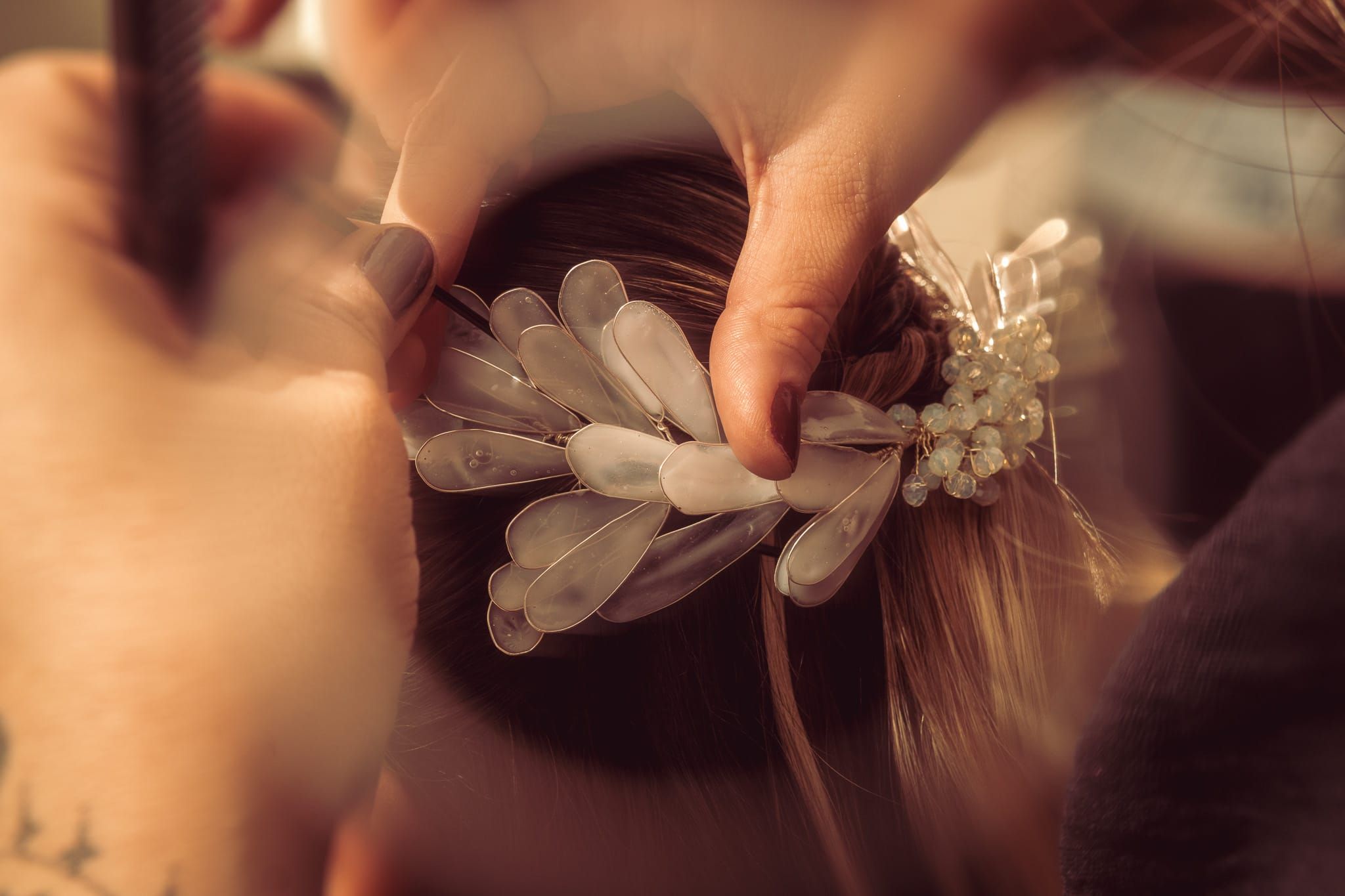 Hands placing a delicate floral hair accessory into a brown updo hairstyle.