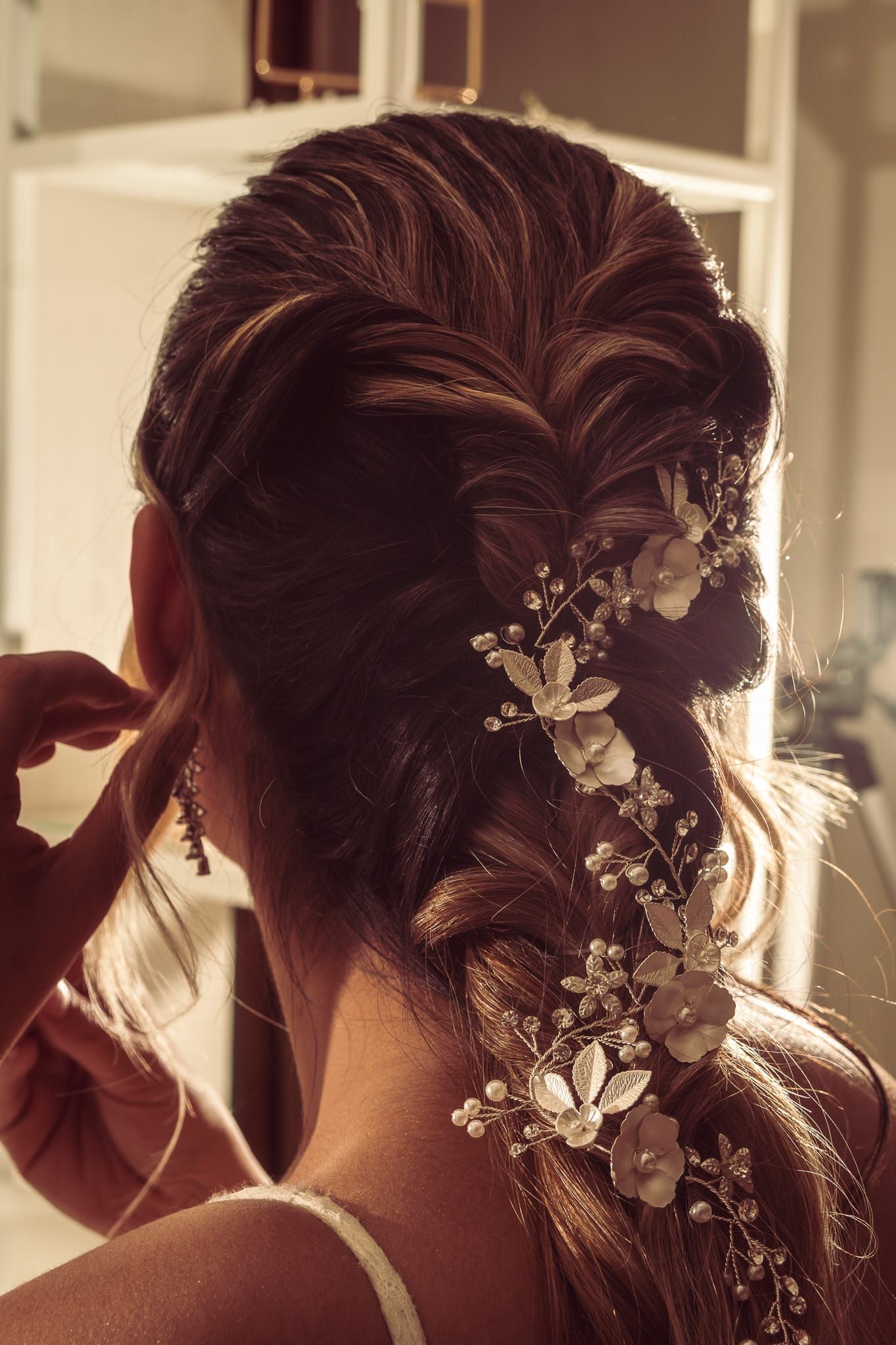 Elegant bridal hairstyle featuring a fishtail braid adorned with delicate floral hair vine and pearl accessories.