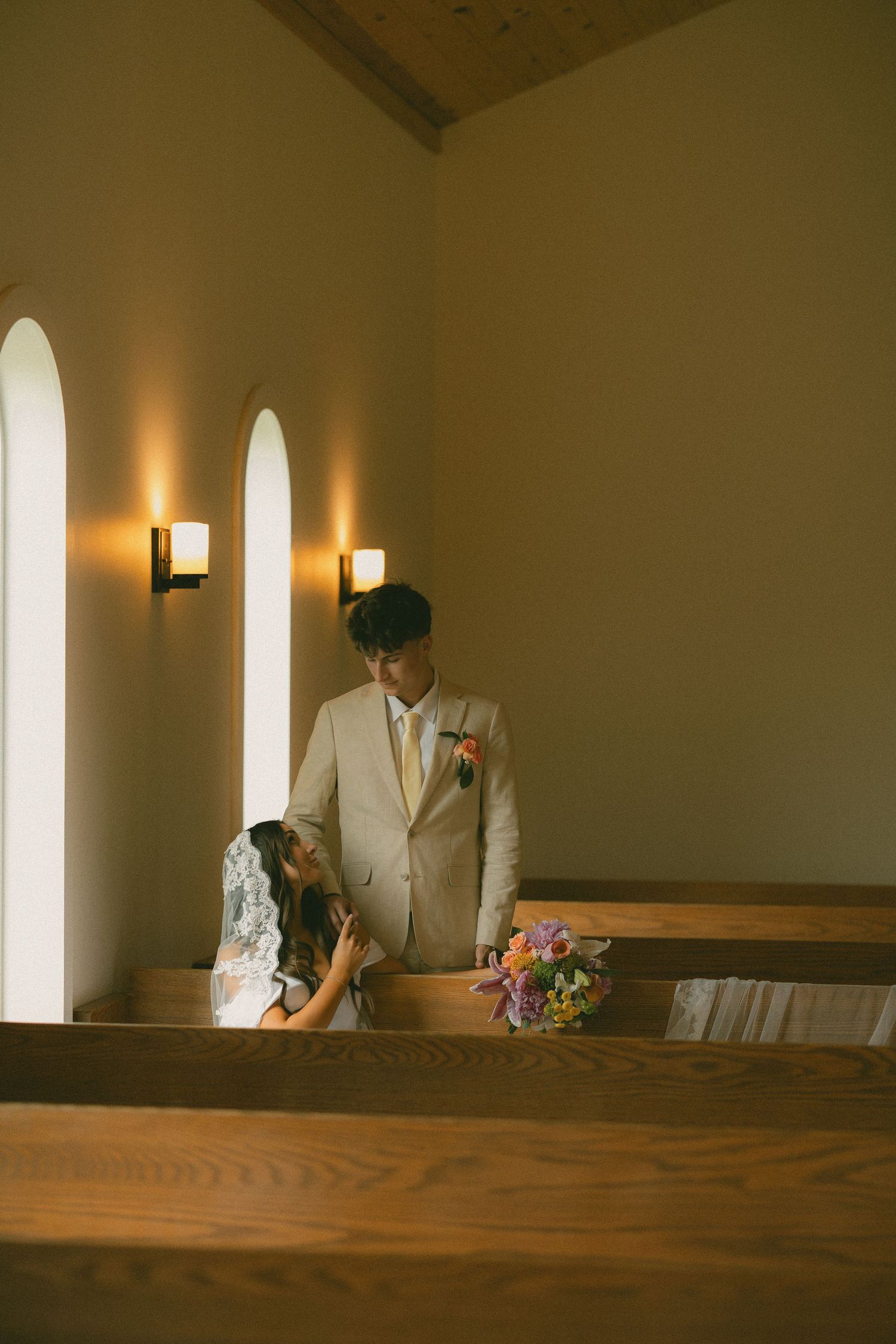 Bride and groom share an intimate moment inside a warmly lit chapel with arched windows.
