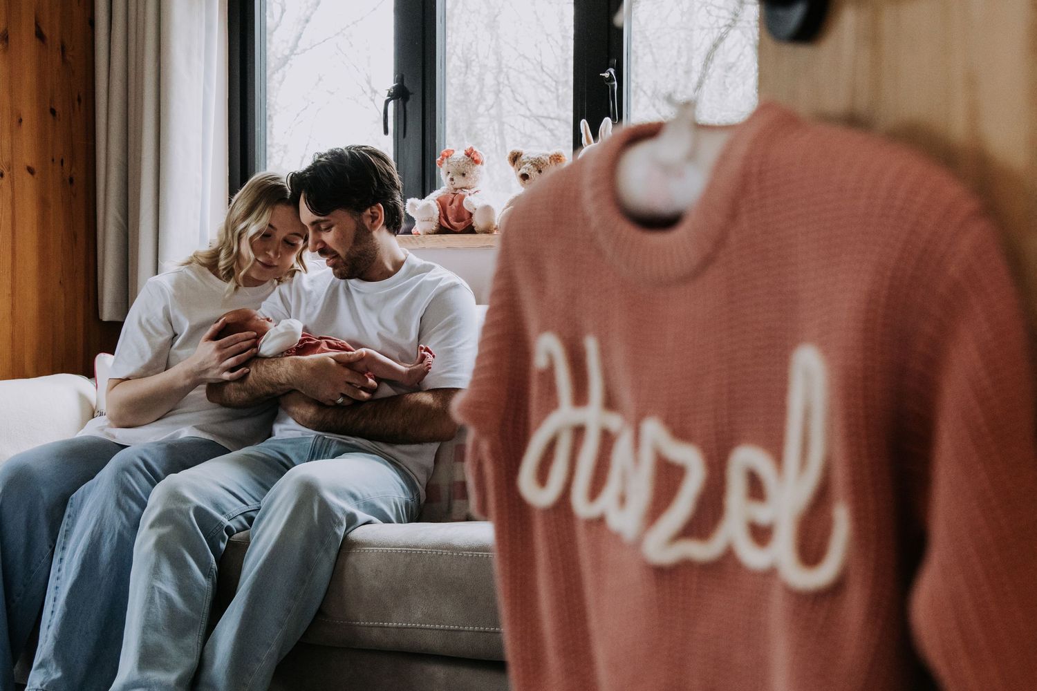 Parents cuddling their newborn baby at home with personalised nursery decor in the foreground.