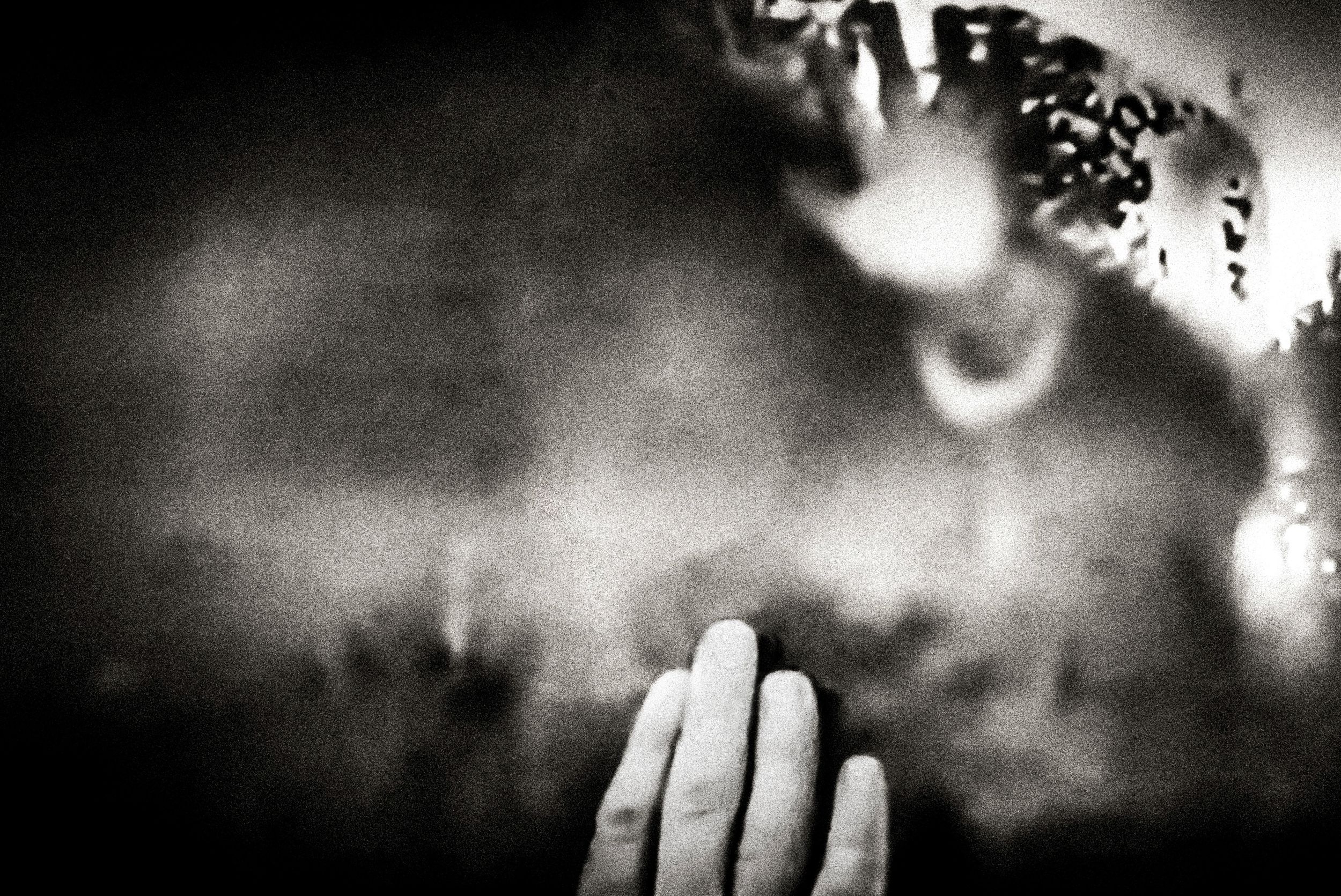 Black and white photo of a hand pressed against glass with blurred figures in the background.